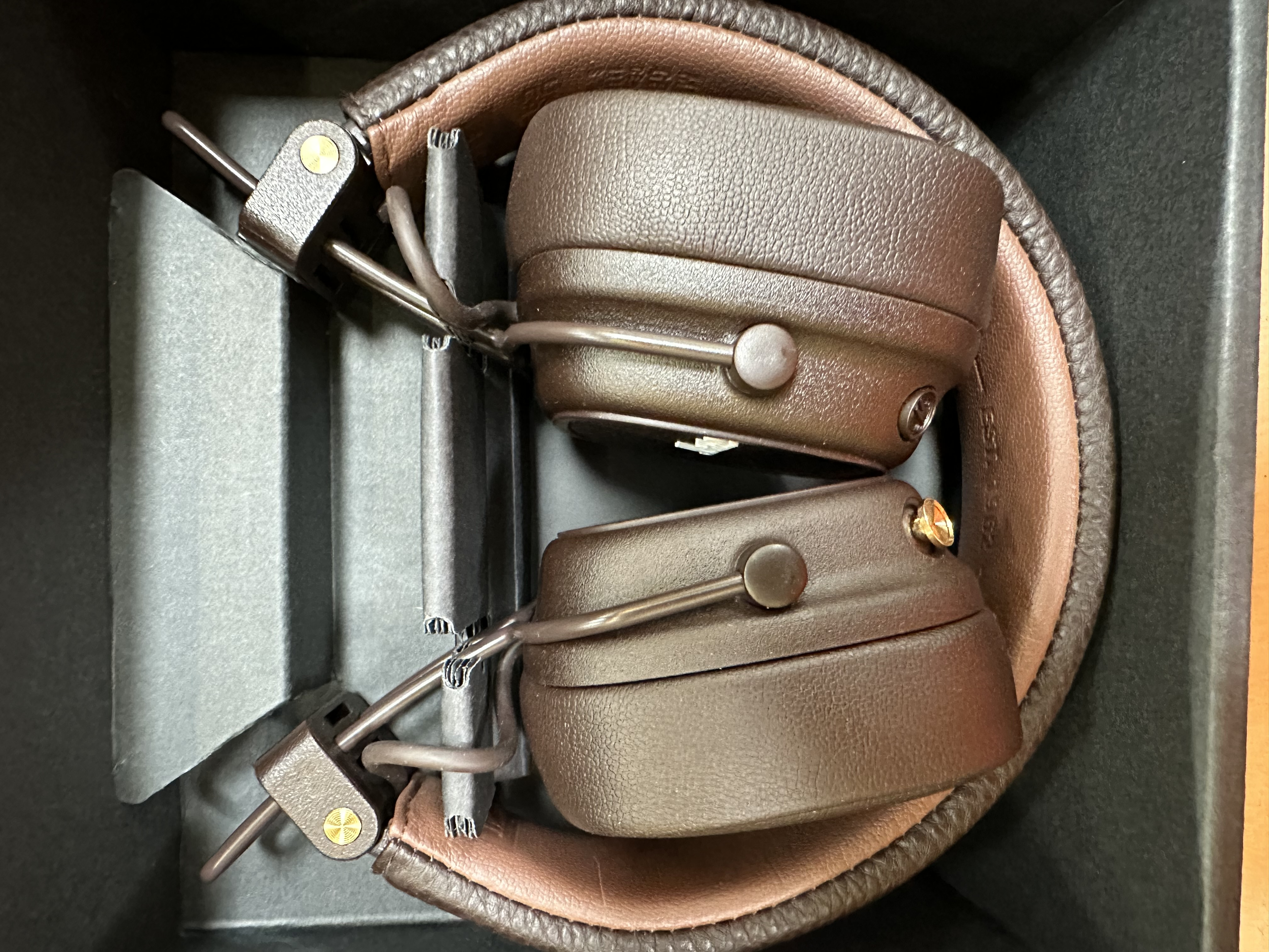 Brązowe słuchawki w pudełku. Zbliżenie, pokazujące nauszniki i pałąk.