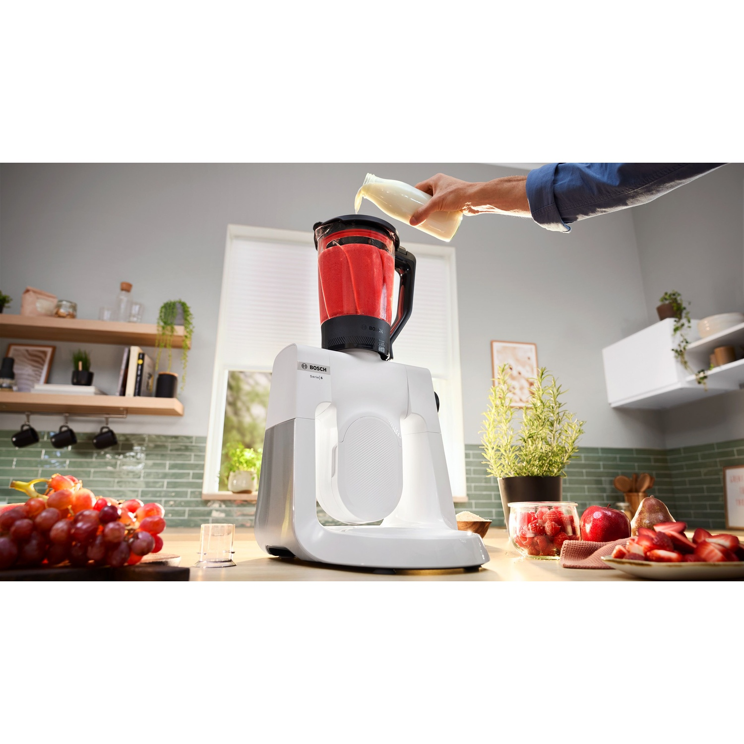 Persona che versa liquido in un frullatore collegato a un elettrodomestico da cucina bianco.