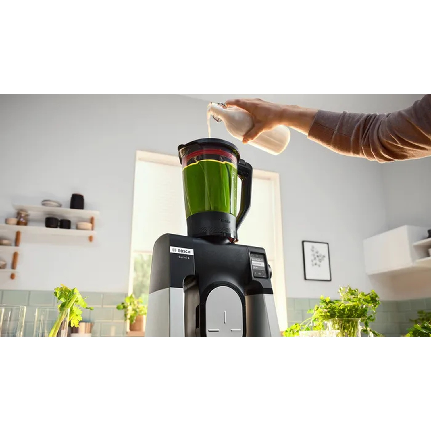 Un frullatore viene riempito con ingredienti verdi, con una persona che versa liquido da una bottiglia.