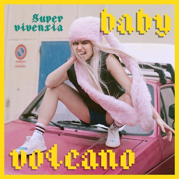 Eine Frau mit Hasenmütze sitzt auf einem Auto. Gelbe Textüberlagerungen: baby, super vivencia, volcano.