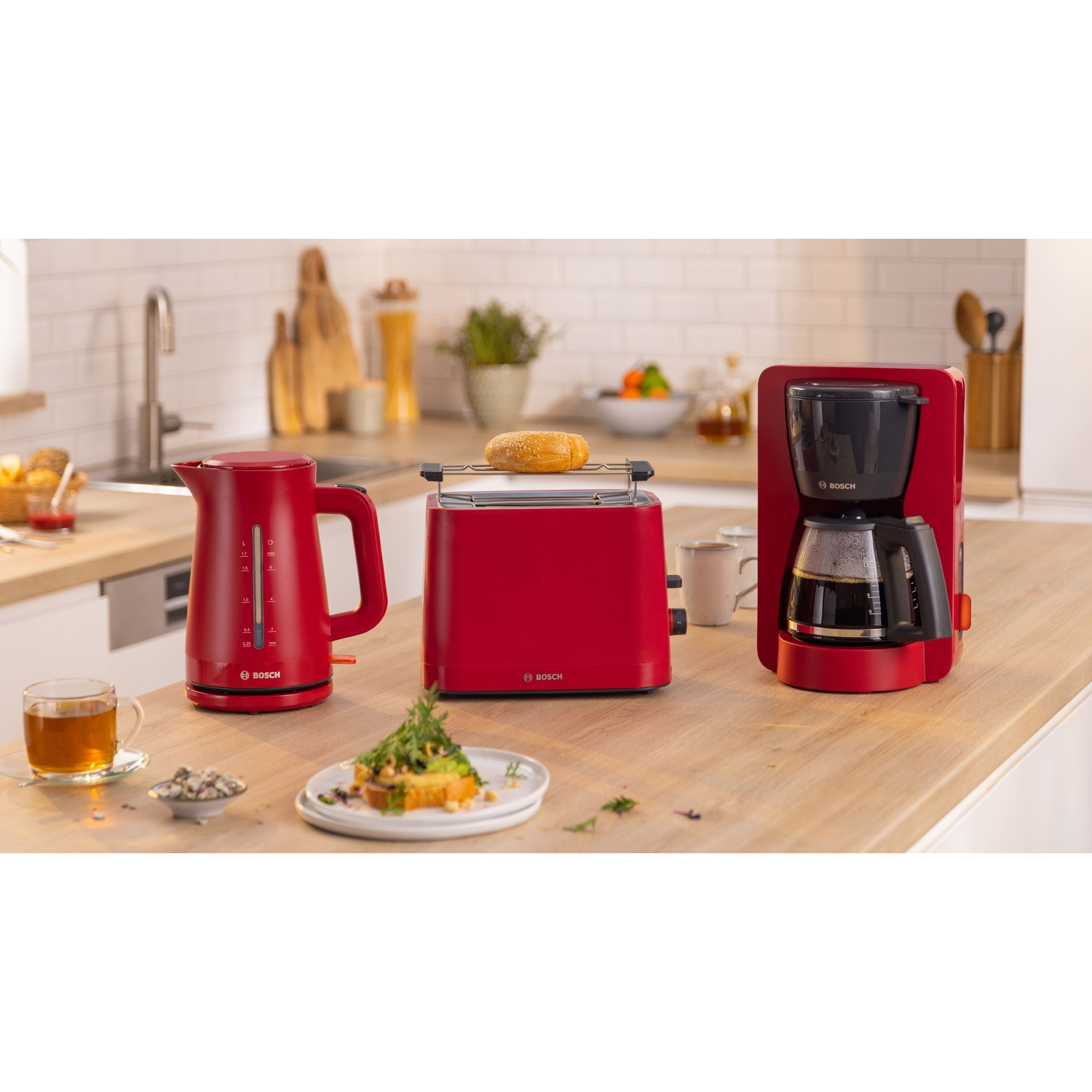 Scena cucina con bollitore, tostapane e macchina per il caffè rossi. Toast e cibo presenti sul bancone.