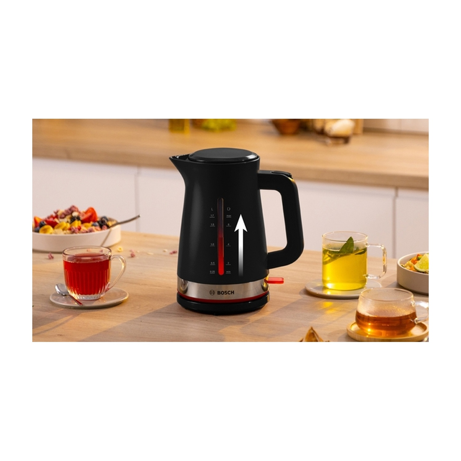 Bollitore nero con base rossa, freccia verso l'alto. Tazze con bevande e frutta sul tavolo.