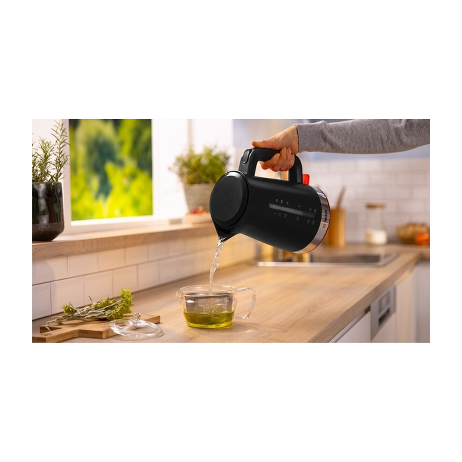 Una persona versa acqua da un bollitore nero in una tazza da tè di vetro.