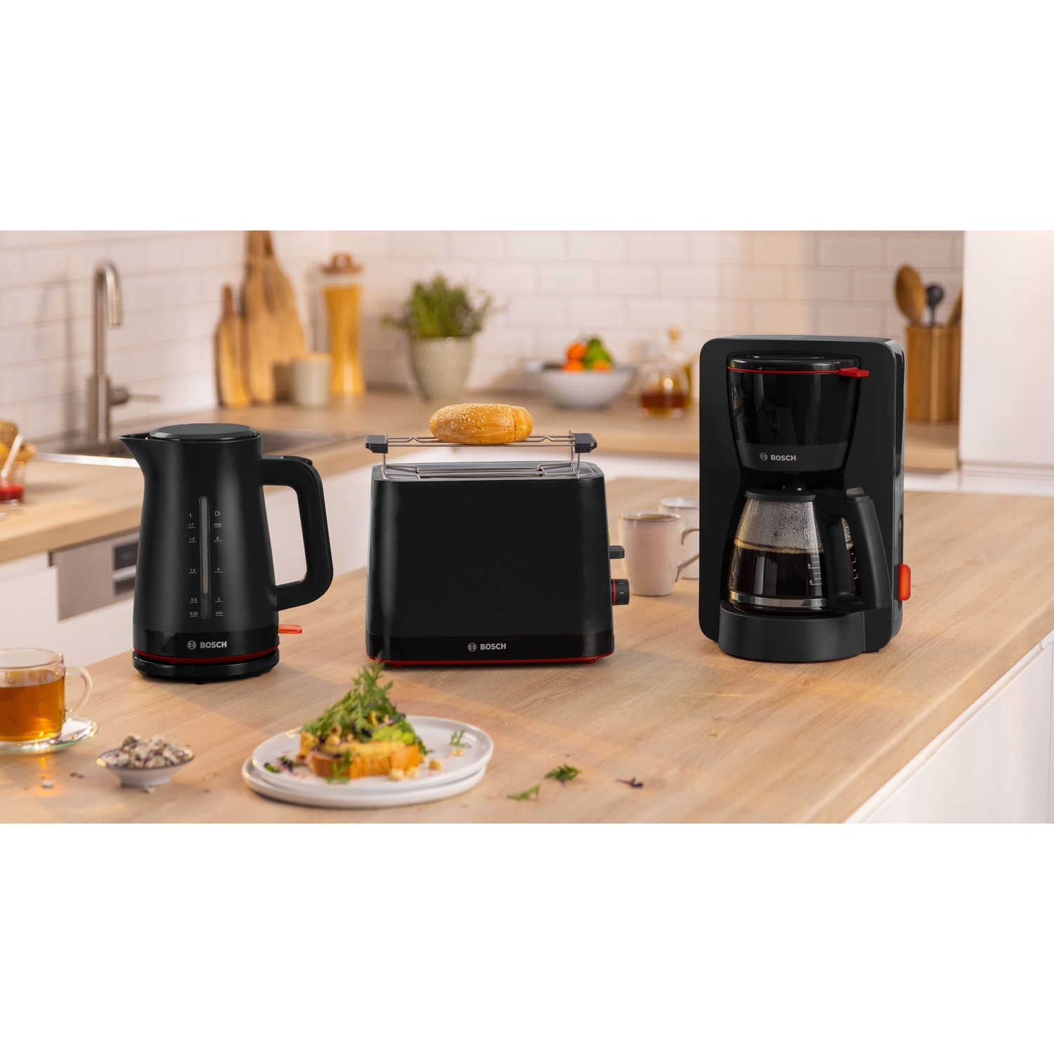 Elettrodomestici da cucina Bosch neri: bollitore, tostapane con toast e macchina per il caffè su superficie in legno.