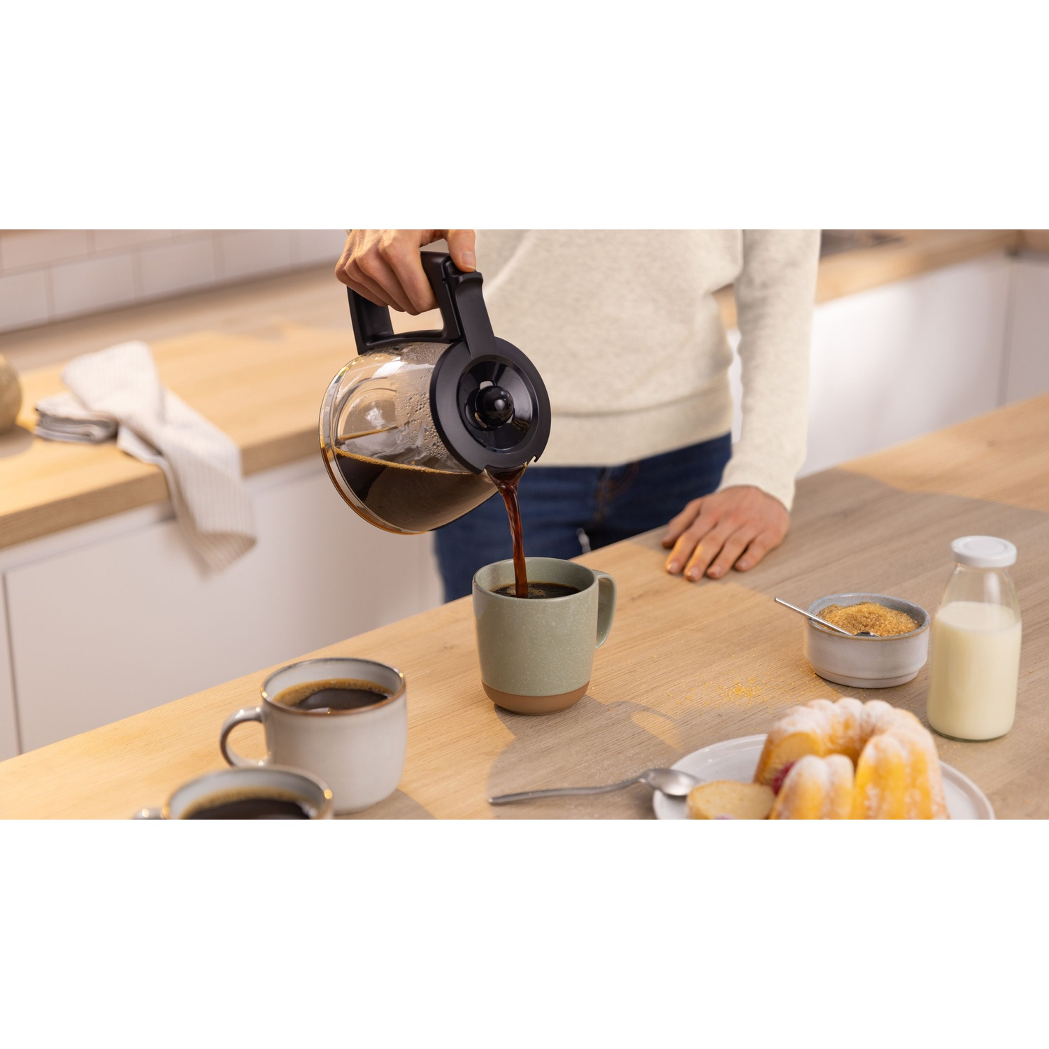 Persona che versa caffè in una tazza, con altri elementi di caffè su un tavolo.