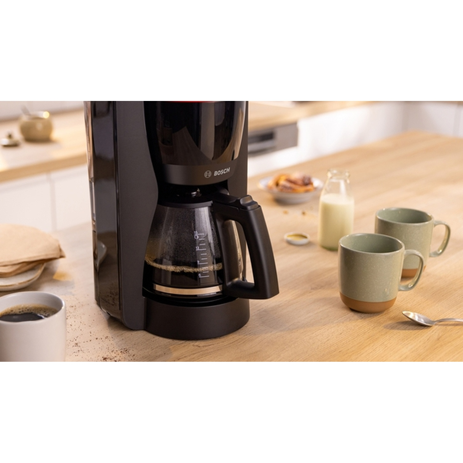 Macchina da caffè con caffè nella caraffa. Tazze da caffè e latte sono sul tavolo di legno.