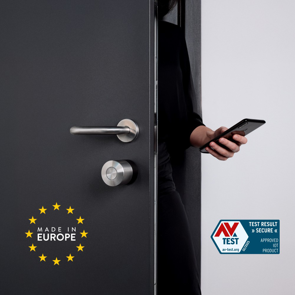 Egy személy egy telefont használva nyit ki egy ajtót. Az ajtón okos zár és 'Made in Europe' matrica van.