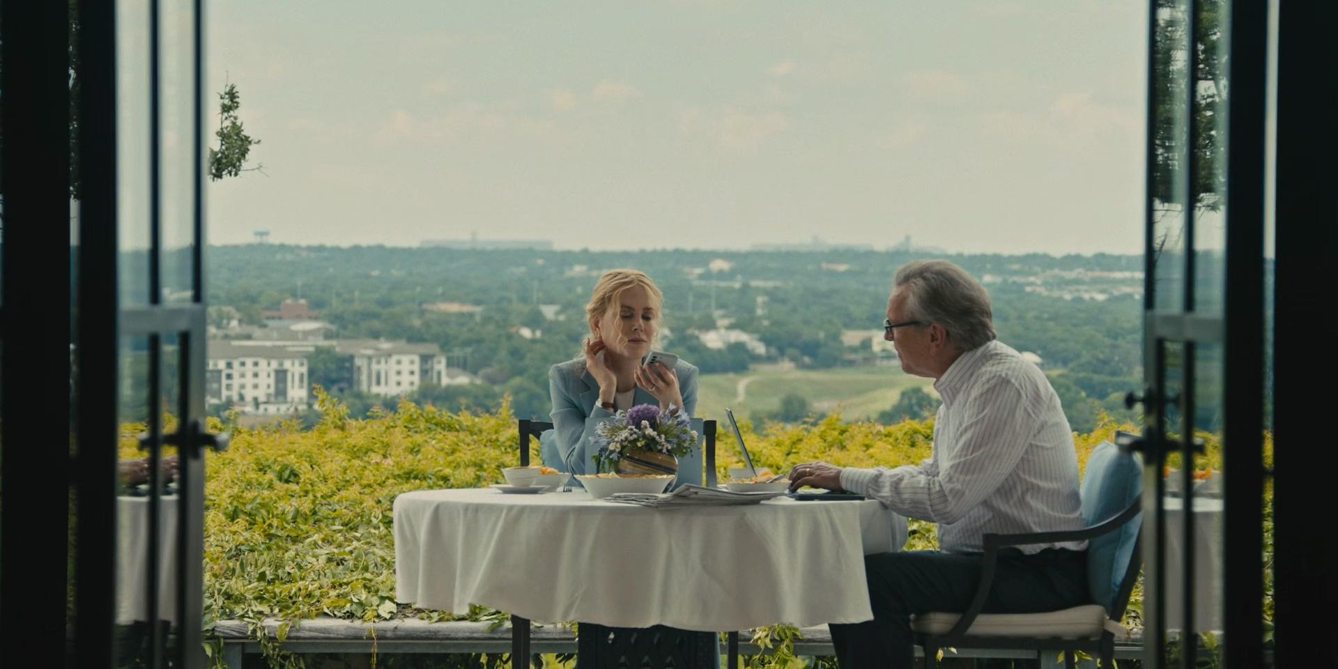 Zwei Personen an einem Tisch im Freien mit Blick auf eine Stadt.
