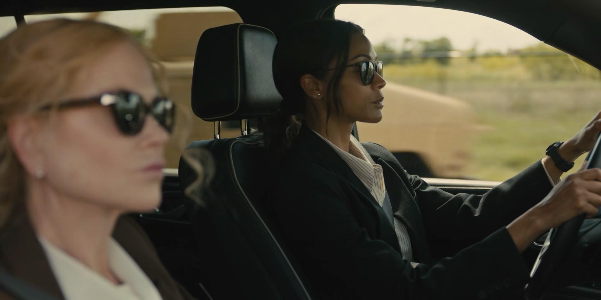 Zwei Frauen in einem Auto tragen Sonnenbrillen. Eine fährt, die andere schaut nach vorne.