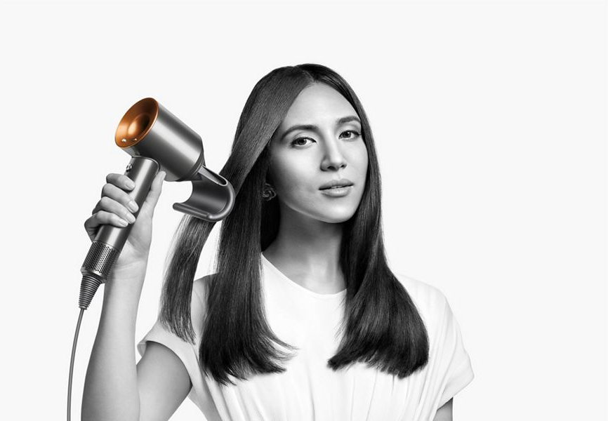 Femme utilisant un sèche-cheveux argenté et doré.