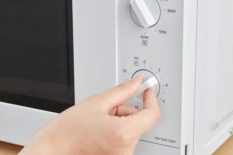 Une main tourne le bouton de minuterie d'un four à micro-ondes blanc.