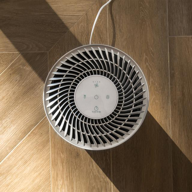 A légtisztító kerek, szellőzőnyílásokkal és gombokkal. Fa padló.