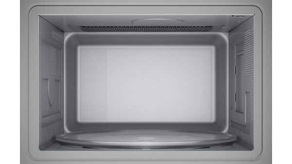 Vista interior de un horno microondas. Interior vacío con plato giratorio de cristal. Paredes grises.