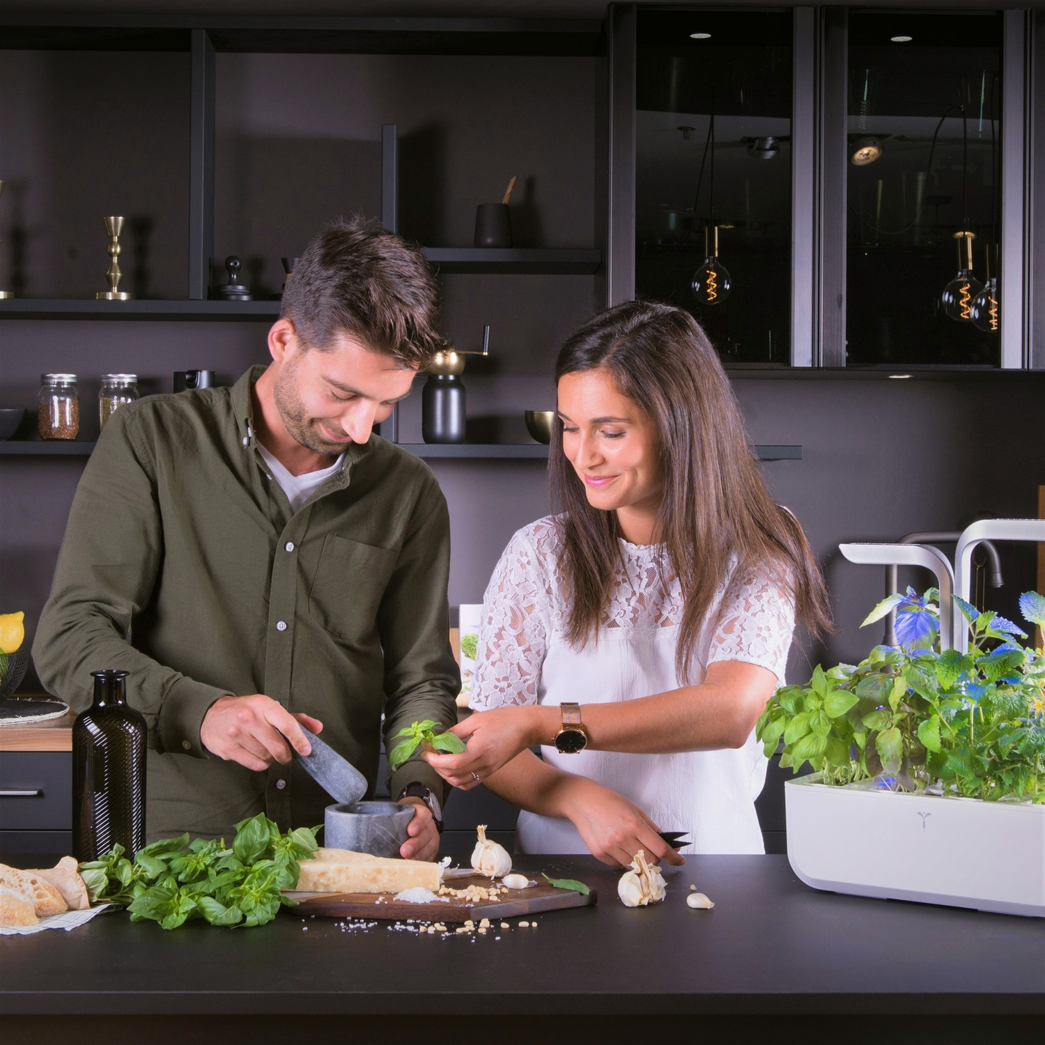 Una coppia prepara il cibo in una cucina con erbe e verdure sul bancone.