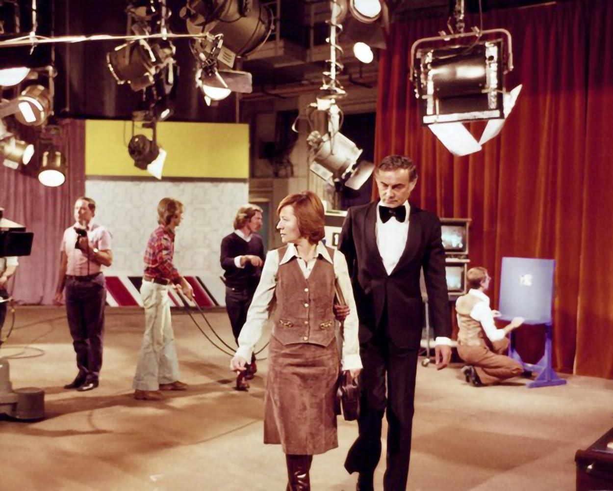 Ein Filmset mit einem Paar, das spazieren geht. Mehrere Crewmitglieder befinden sich im Hintergrund mit Lichtern und Ausrüstung.
