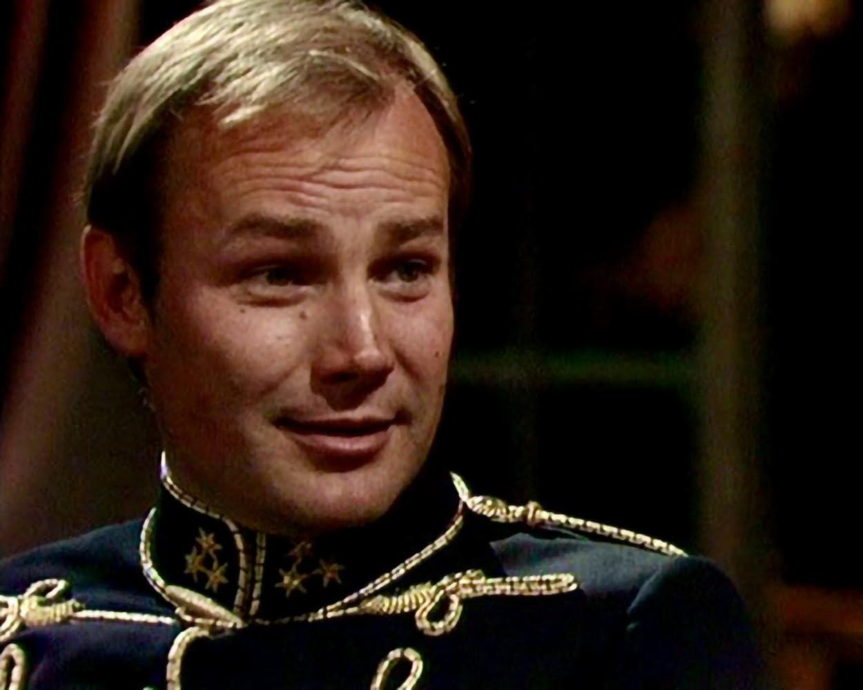 Mann in Uniform mit goldenen Akzenten und einem lächelnden Gesicht.
