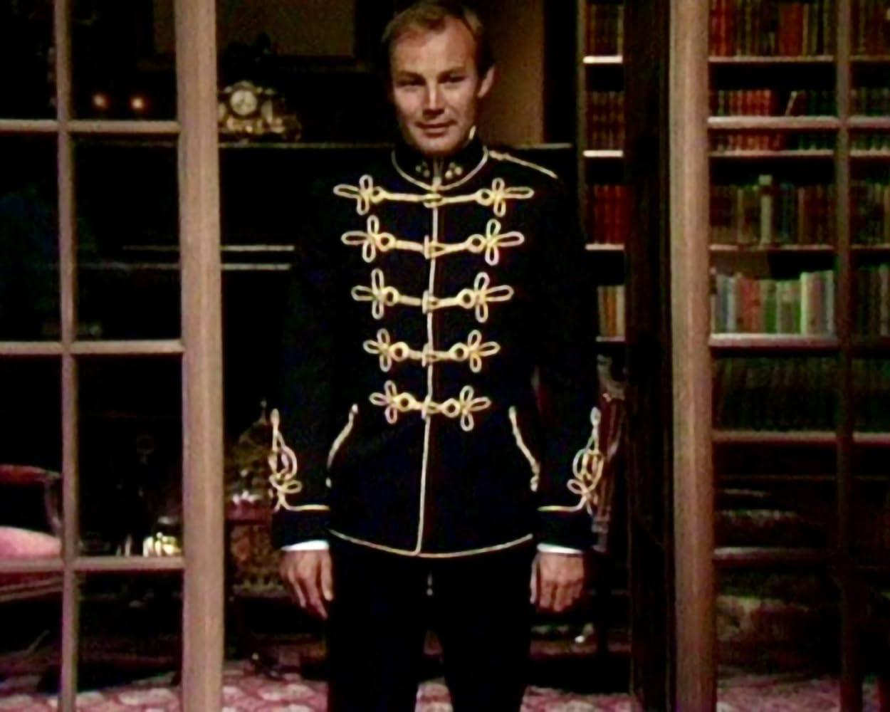 Mann in formeller Militärjacke, stehend in einem Raum mit Bücherregalen.