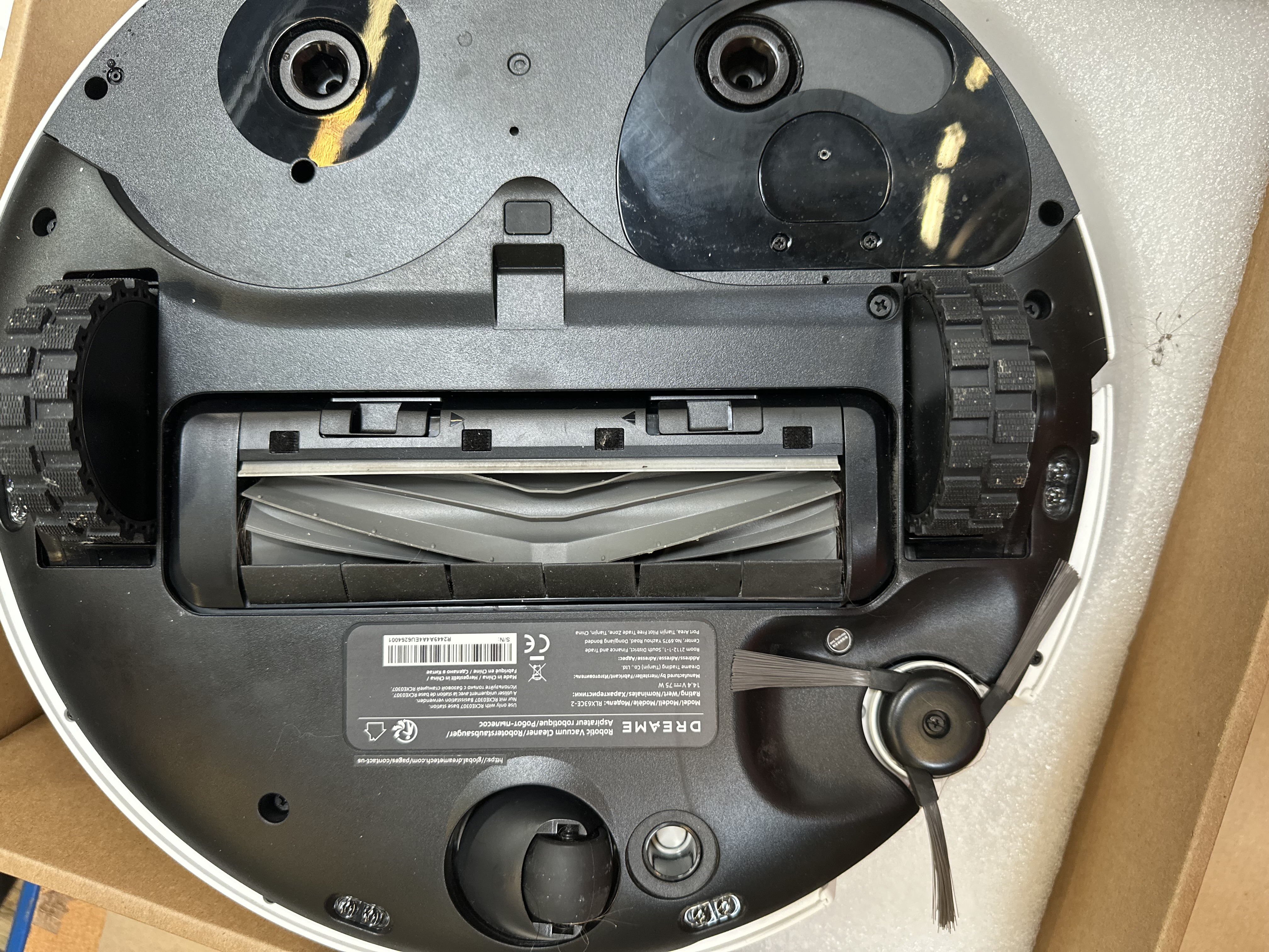 Widok od spodu robota sprzątającego. Pokazuje koła, szczotki i elementy wewnętrzne.