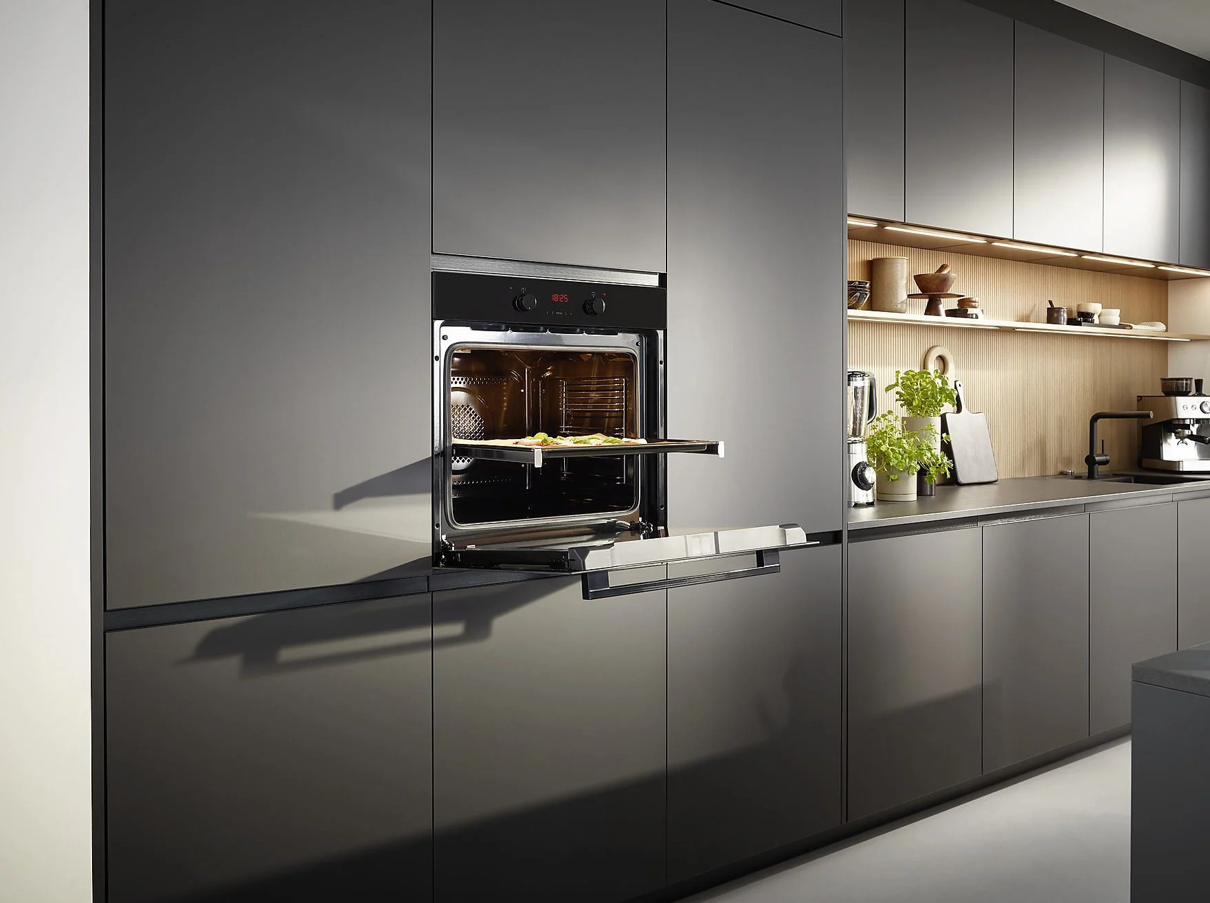 Nowoczesna szara kuchnia z otwartymi drzwiami piekarnika, ukazująca tacę z jedzeniem w środku.