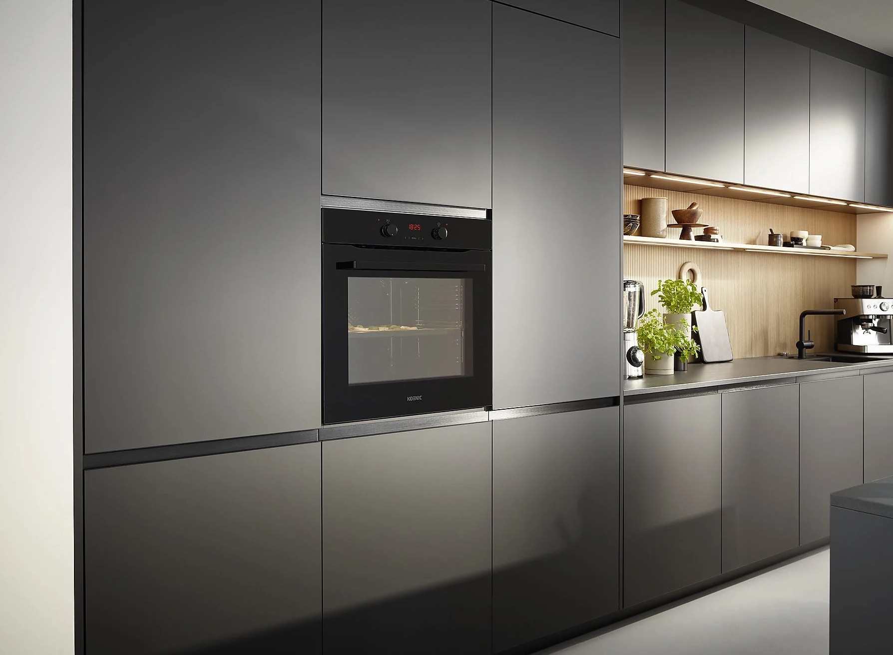 Nowoczesna kuchnia z piekarnikiem do zabudowy. Ciemnoszare szafki, drewniane półki. Piekarnik jest czarny.