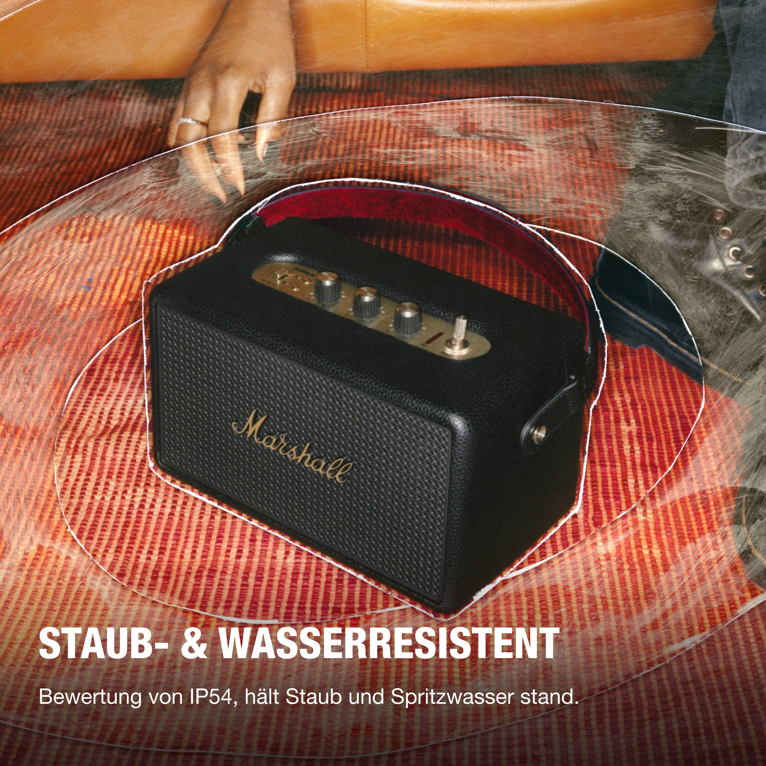Schwarzer tragbarer Marshall-Lautsprecher mit goldfarbenen Knöpfen, auf roter Oberfläche.