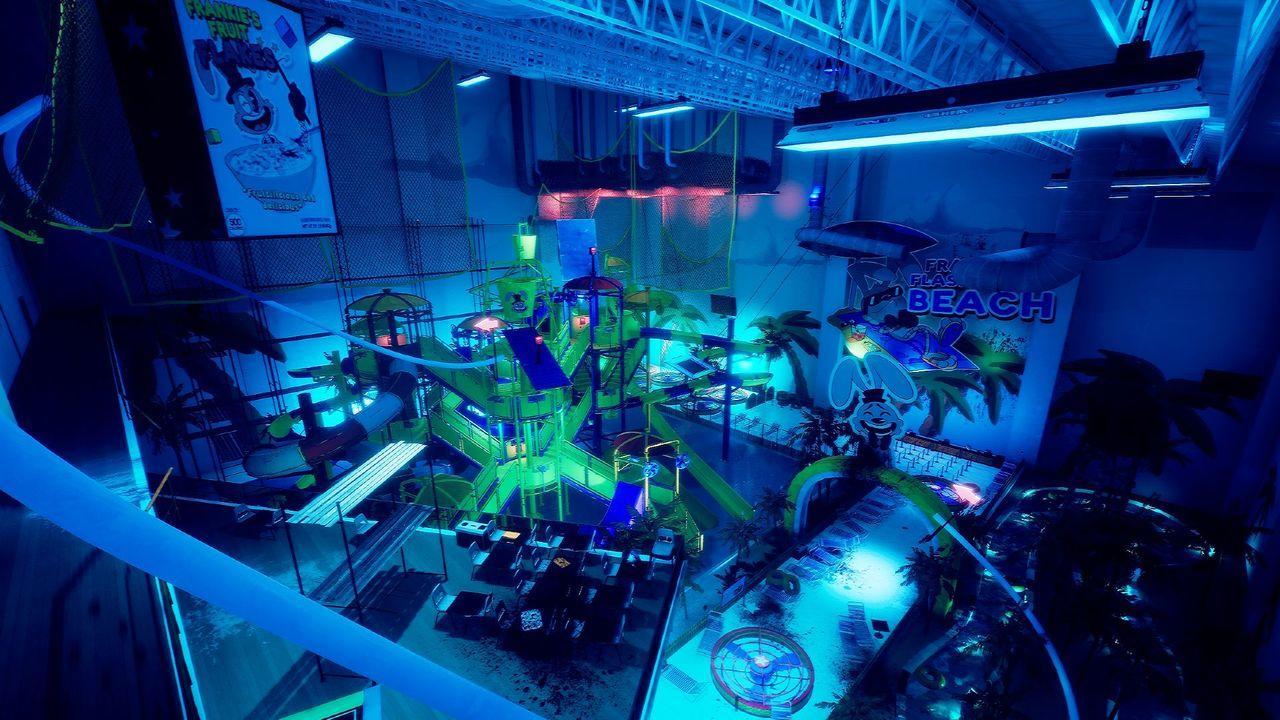 Indoor-Wasserpark mit Rutschen, Becken und Palmen, beleuchtet mit grünen und blauen Lichtern.