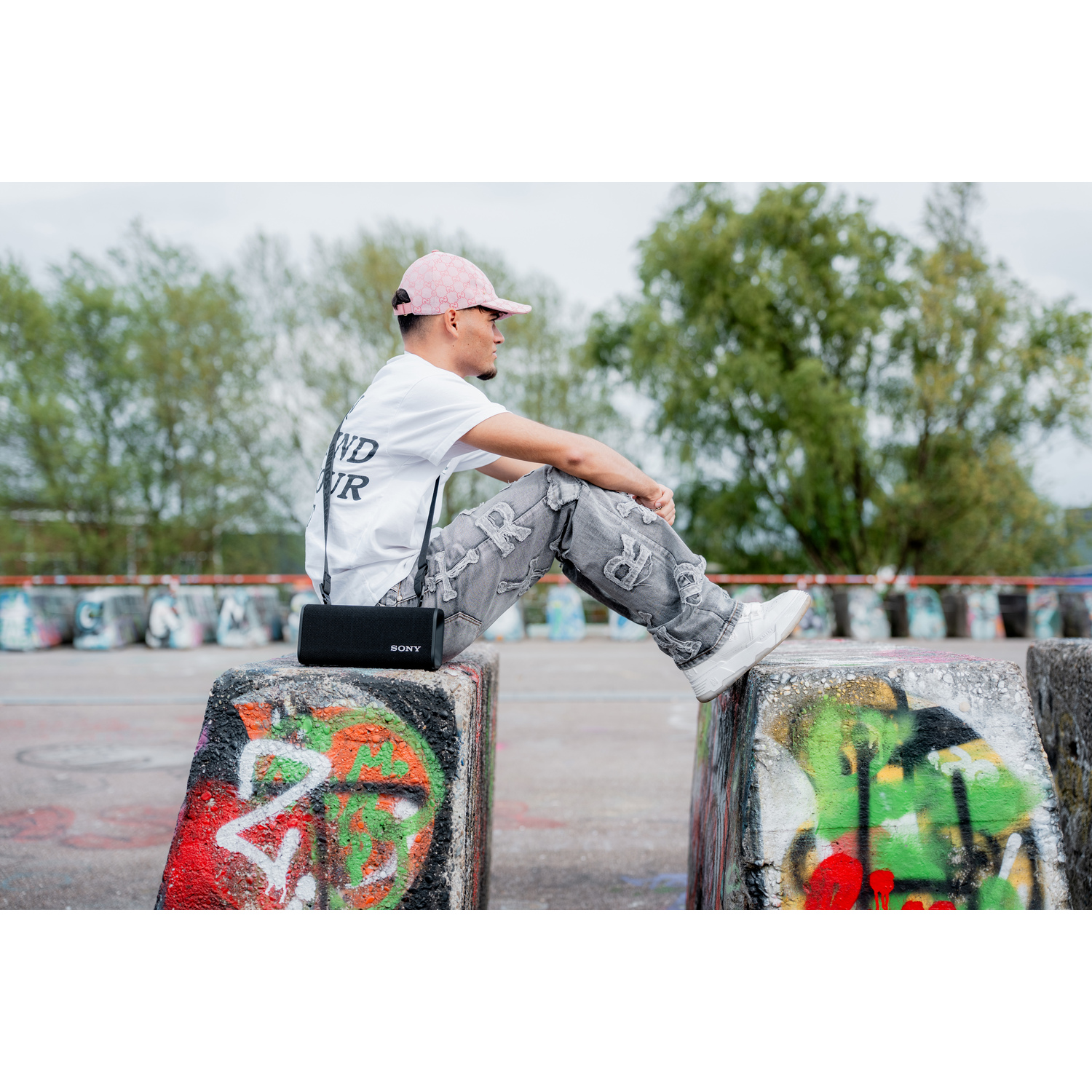 Een man zit op betonnen blokken met een luidspreker en een graffiti-achtergrond.