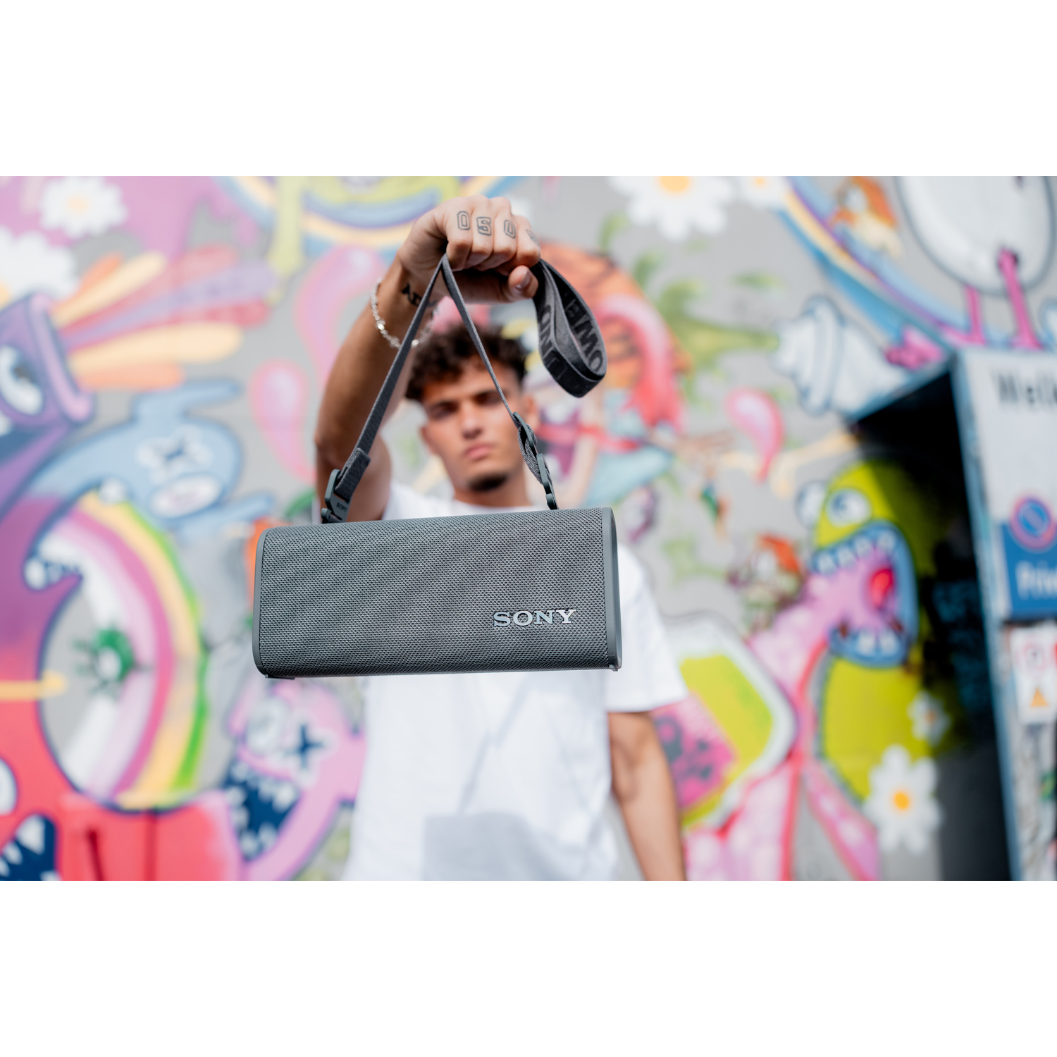 Man houdt grijze Sony-luidspreker vast voor een graffiti-muur.