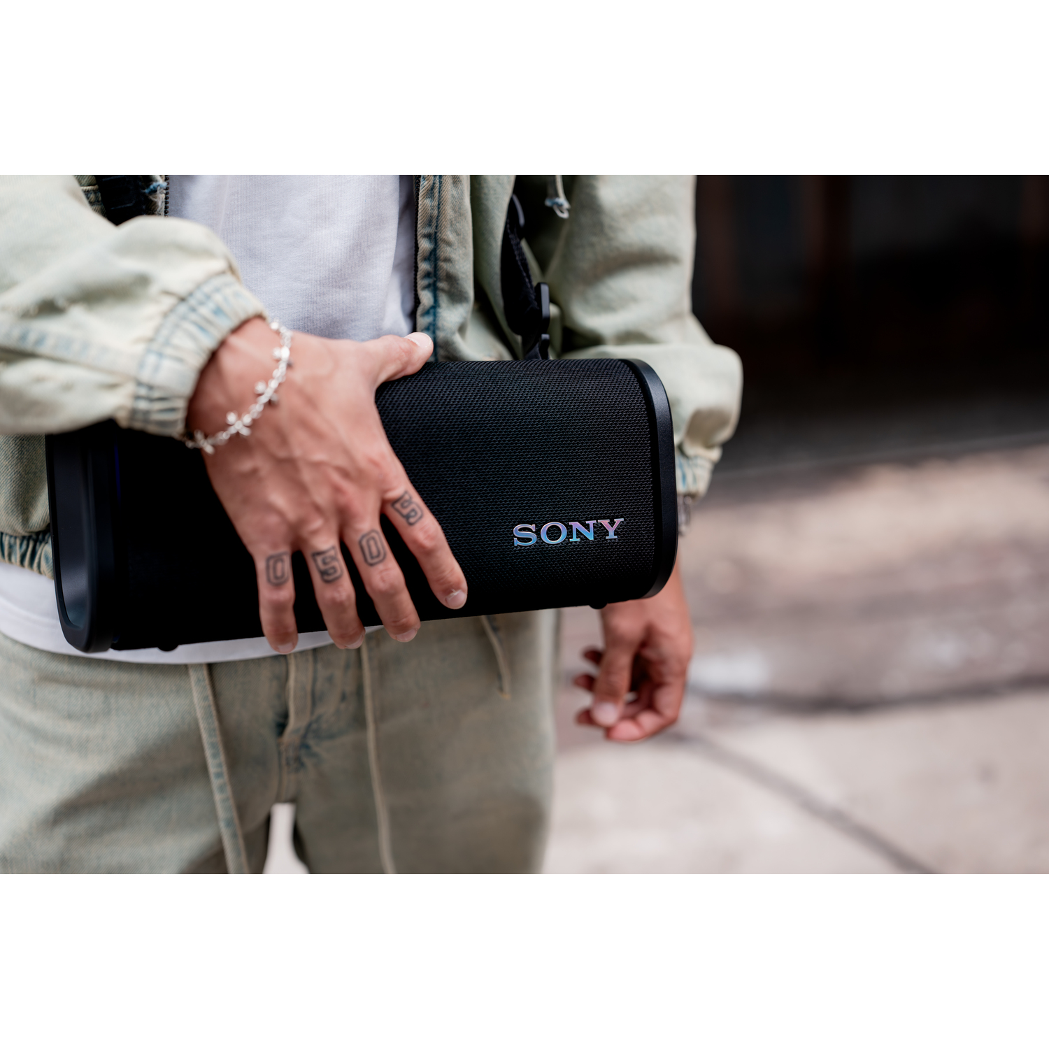 Une personne tenant une enceinte Sony noire avec le logo 'SONY', portant une veste en jean.