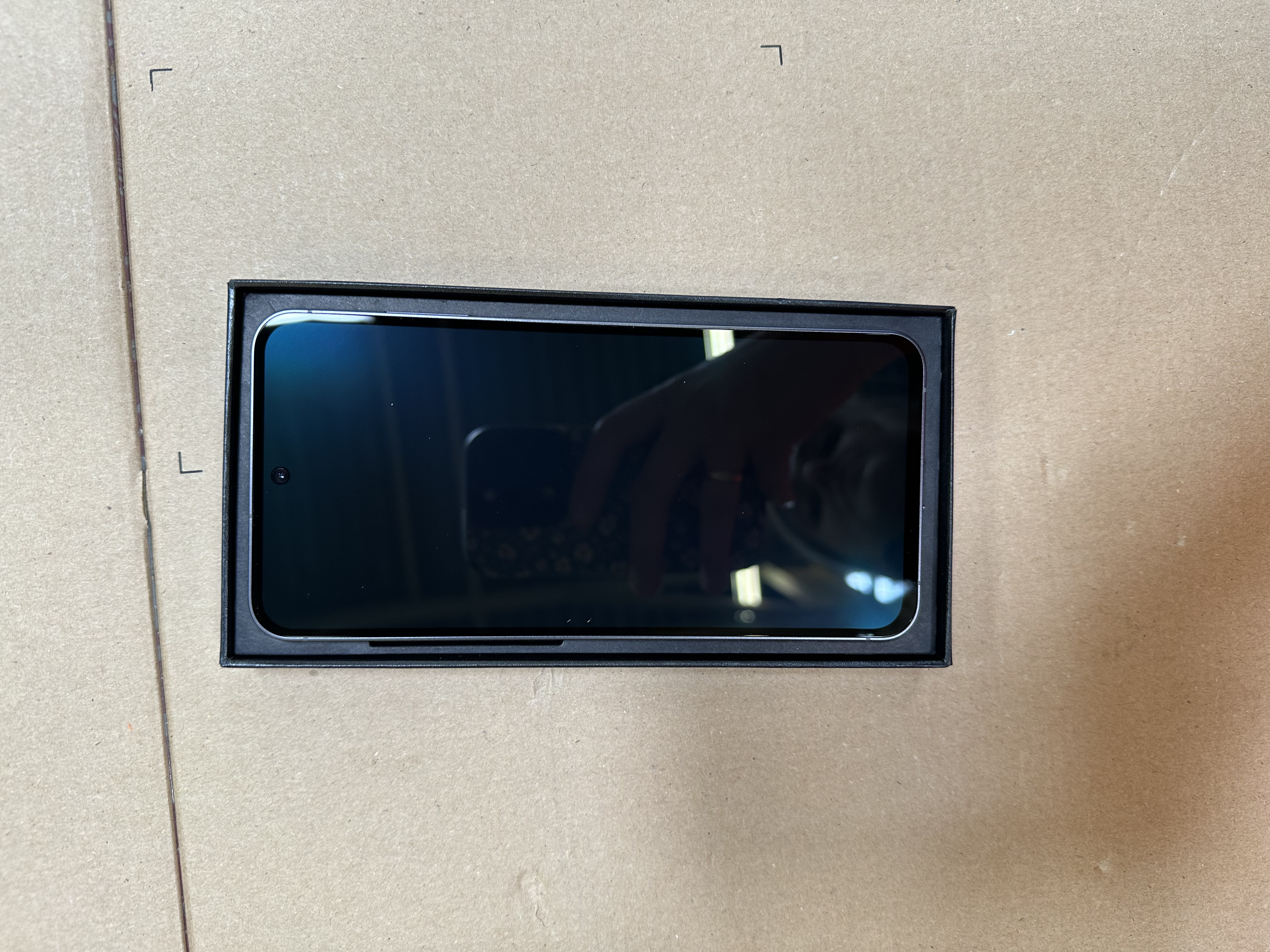 Smartfon z ciemnym ekranem w czarnym pudełku na kartonie.