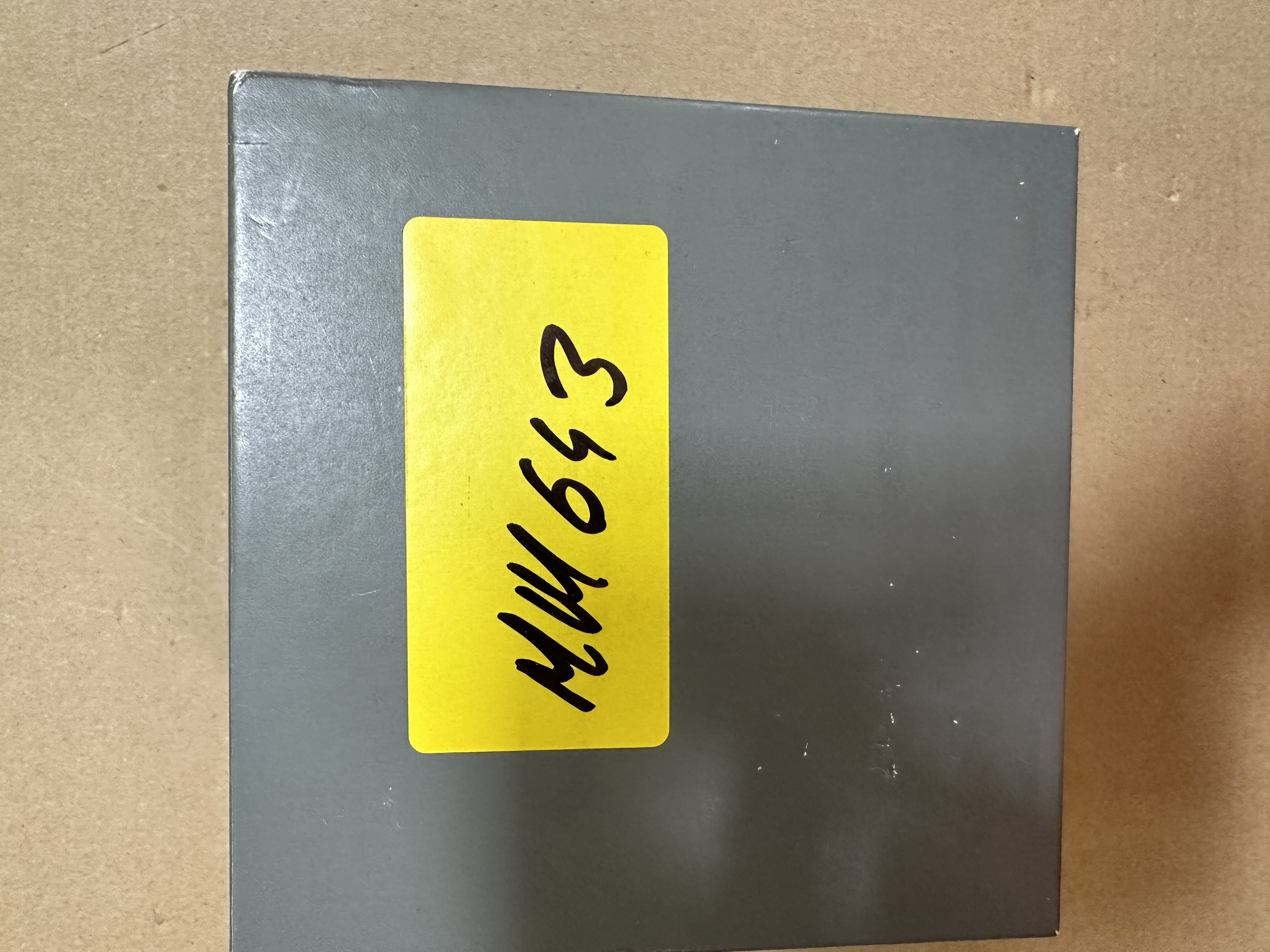 Szare pudełko z żółtą etykietą z odręcznym tekstem.