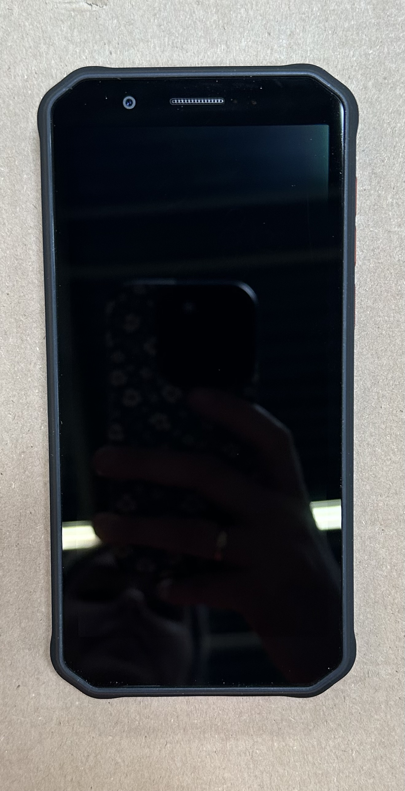 Czarny telefon z czarnym ekranem odbijającym dłoń trzymającą telefon. Widoczny aparat.