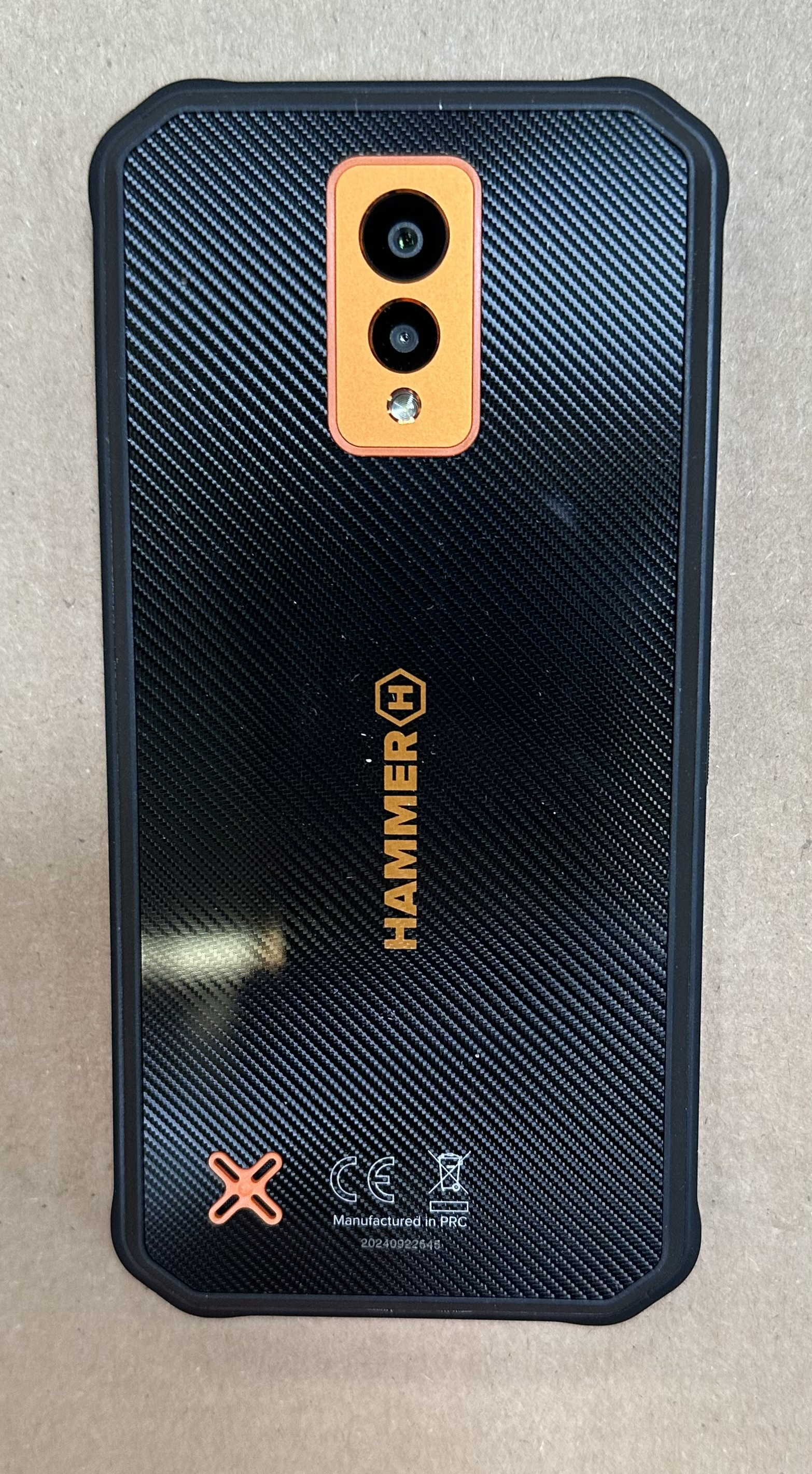 Czarny tył telefonu z teksturowanym wzorem, pomarańczową sekcją aparatu i logo Hammer.