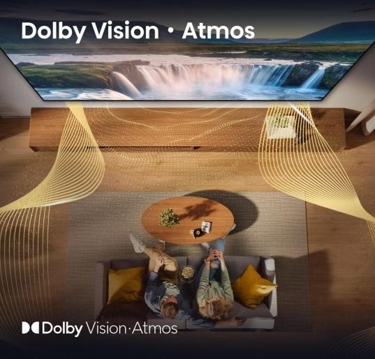 Telewizor na drewnianej szafce, z parą na sofie i logo Dolby Vision Atmos.