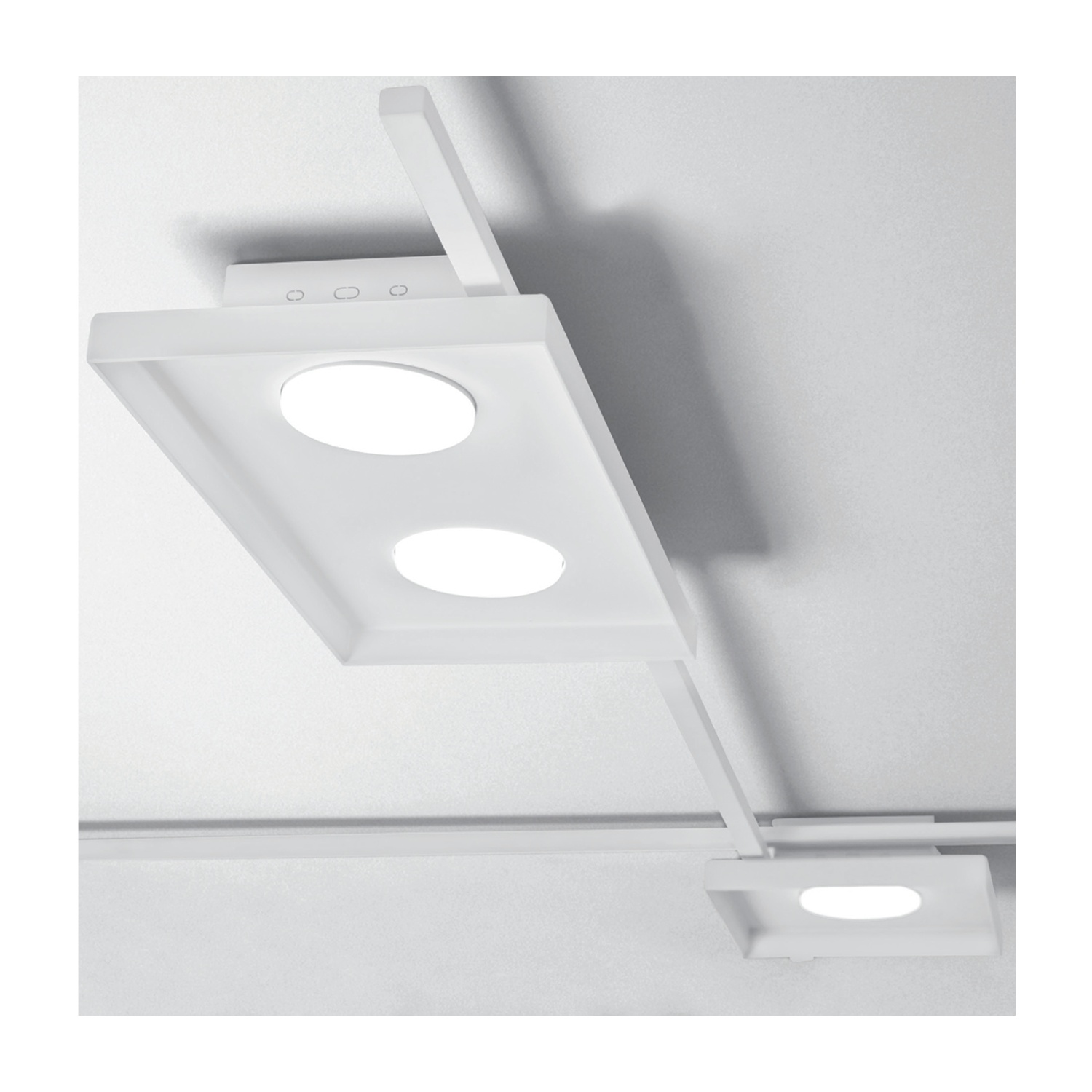 Luci a soffitto bianche su un sistema a binario. Due luci rotonde su un pannello rettangolare. Sfondo bianco.