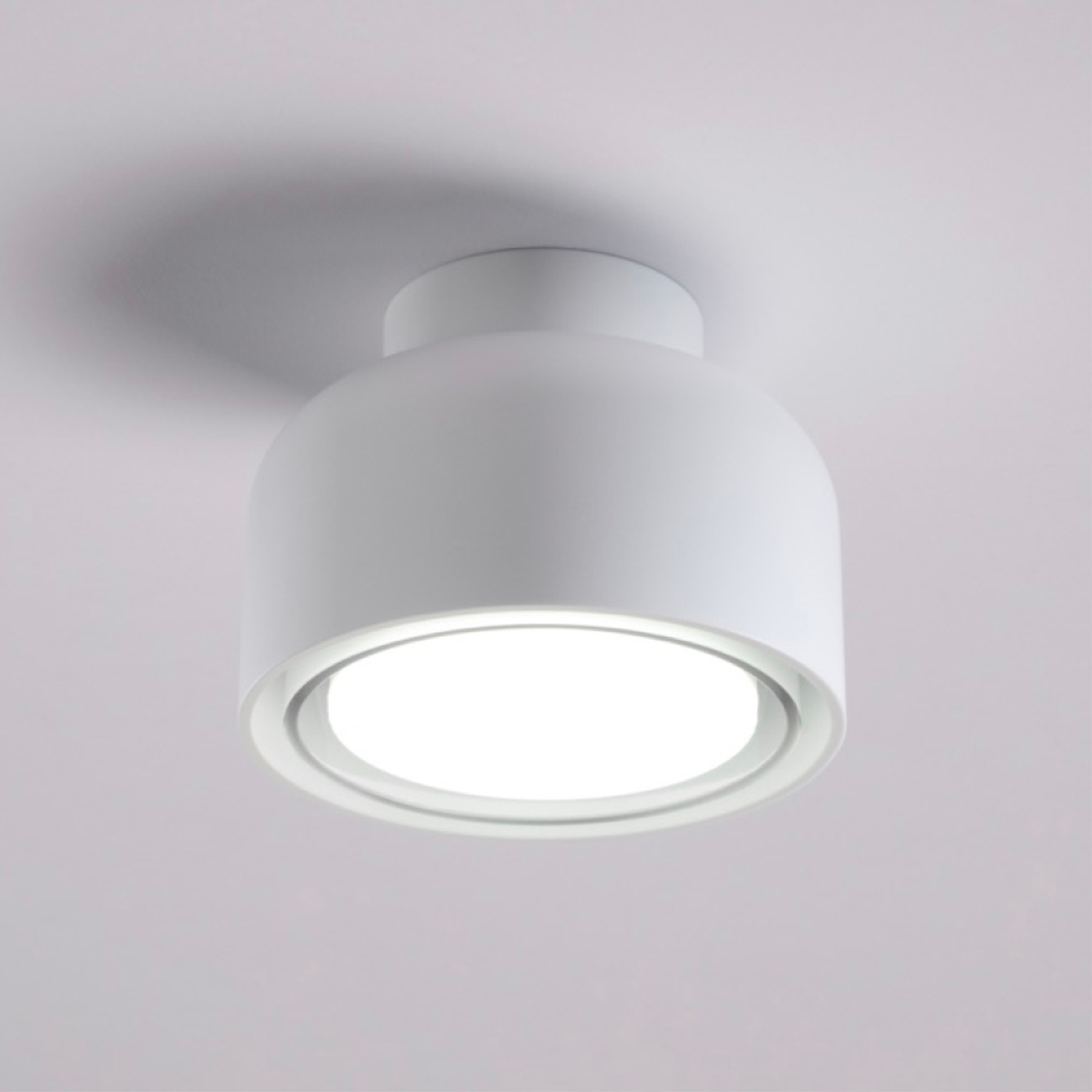 Lampada da soffitto bianca, cilindrica. La base emette luce. Ombra sul soffitto.