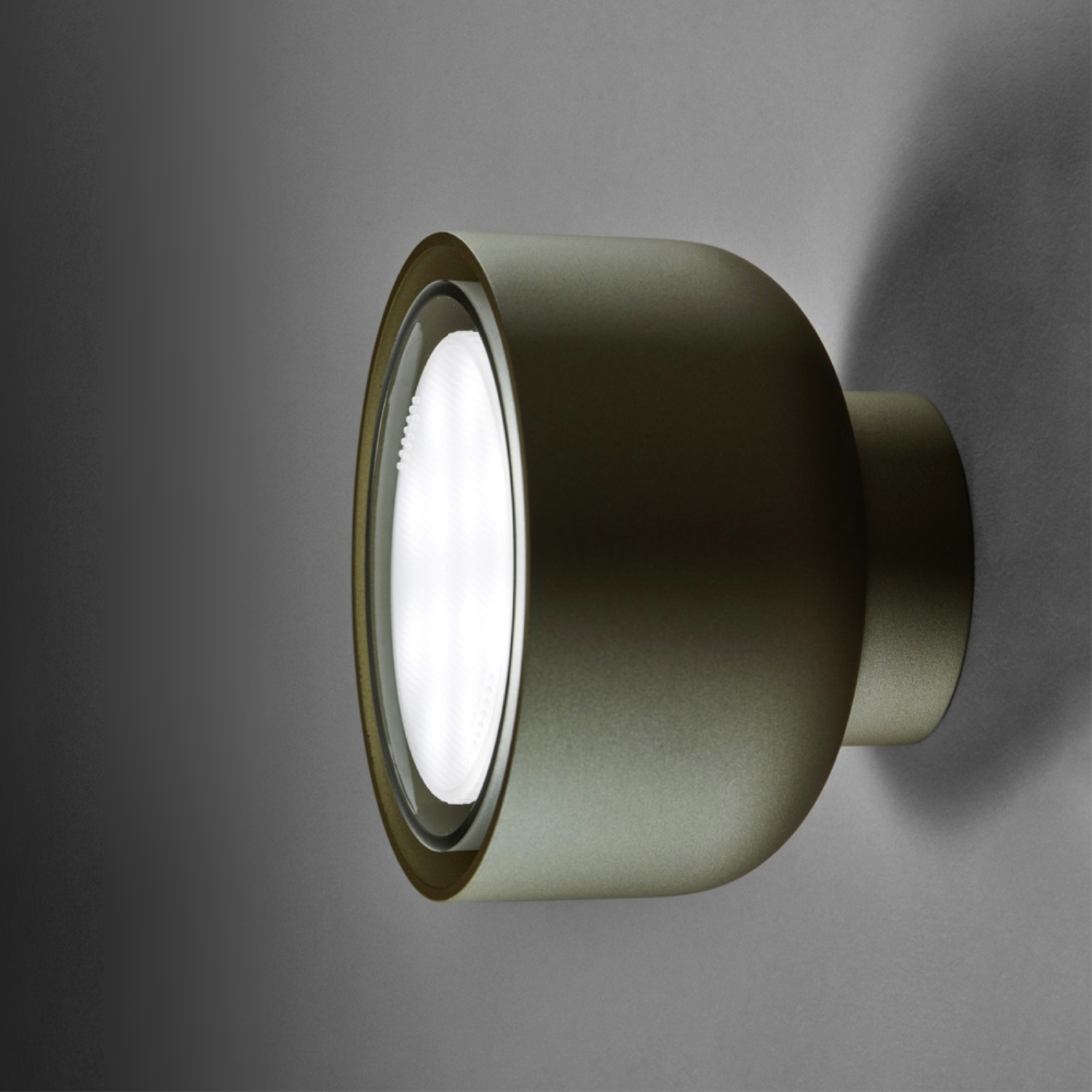 Un moderno apparecchio di illuminazione a soffitto rotondo e scuro. È montato su una parete grigia.