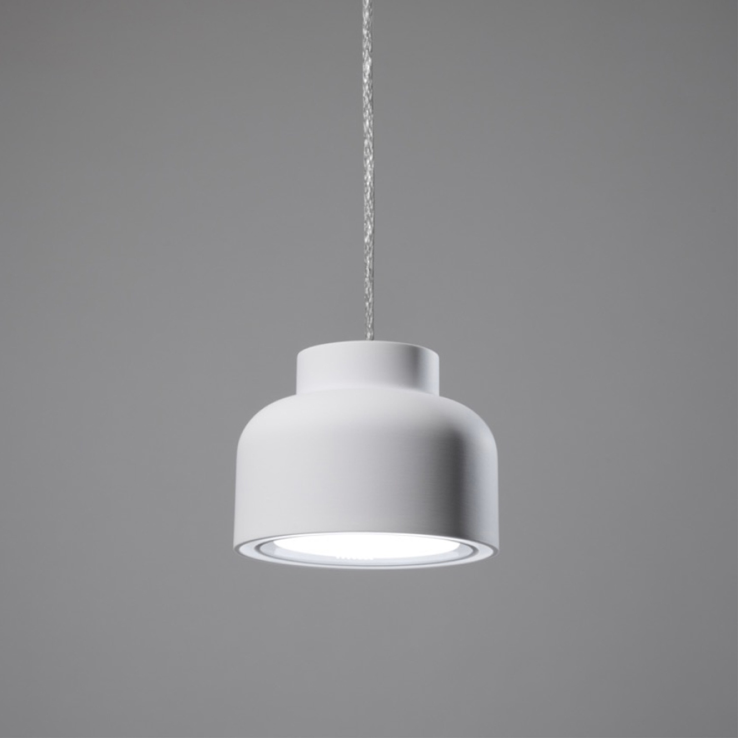 Lampada a sospensione bianca con paralume bianco appesa a un cavo bianco su grigio.