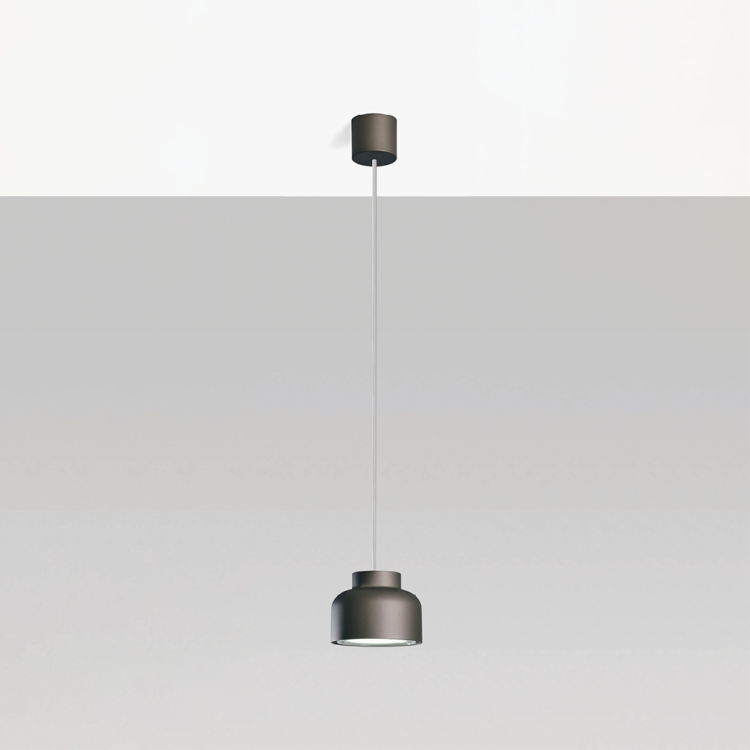 Una lampada a sospensione appesa a un sottile cavo bianco. La luce ha una forma cilindrica grigio scuro.