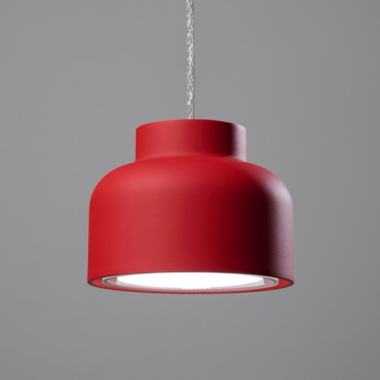 Una lampada a sospensione rossa con una luce bianca che emana dal basso. È appesa su uno sfondo grigio.