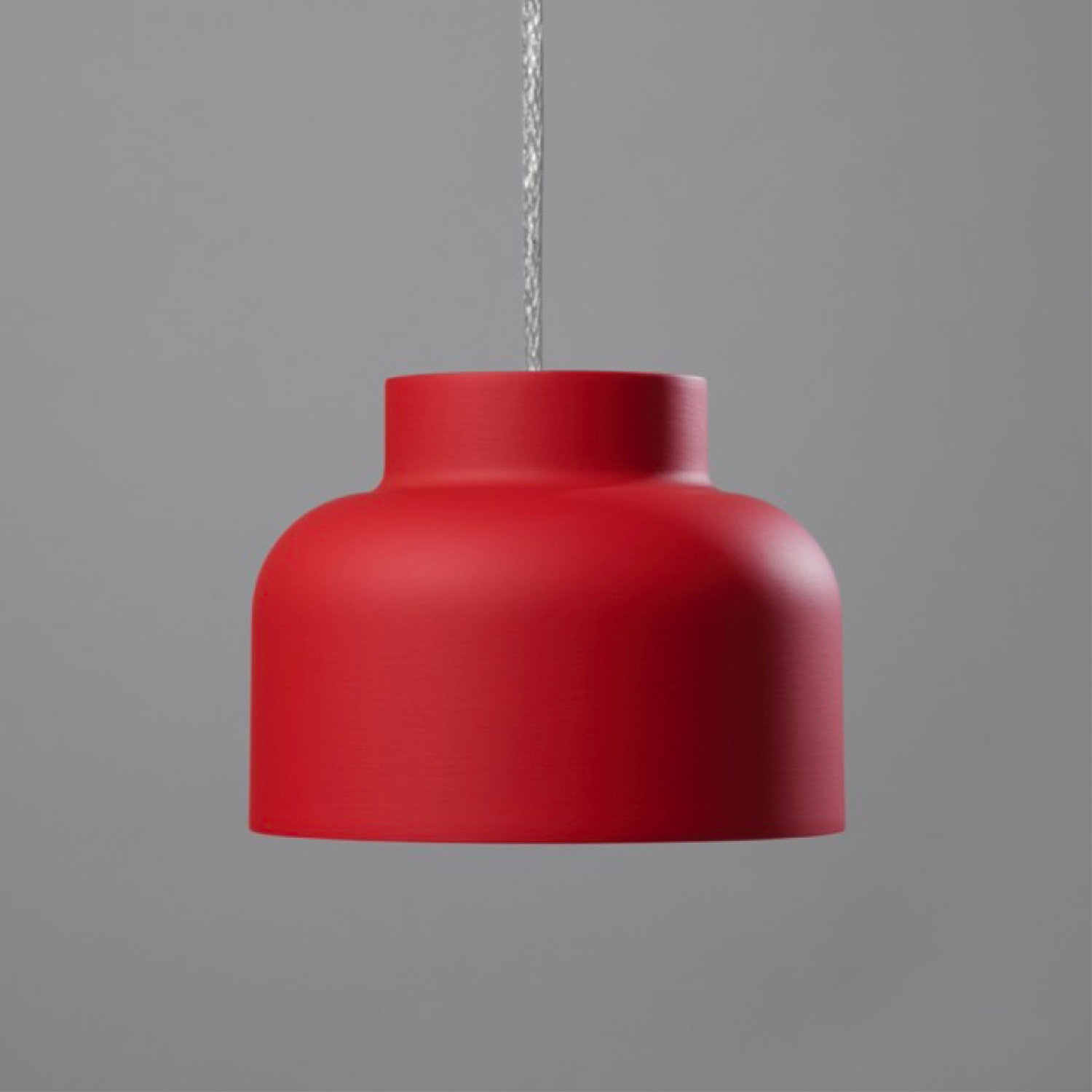 Lampada a sospensione rossa: forma cilindrica, appesa a un cavo su sfondo grigio.
