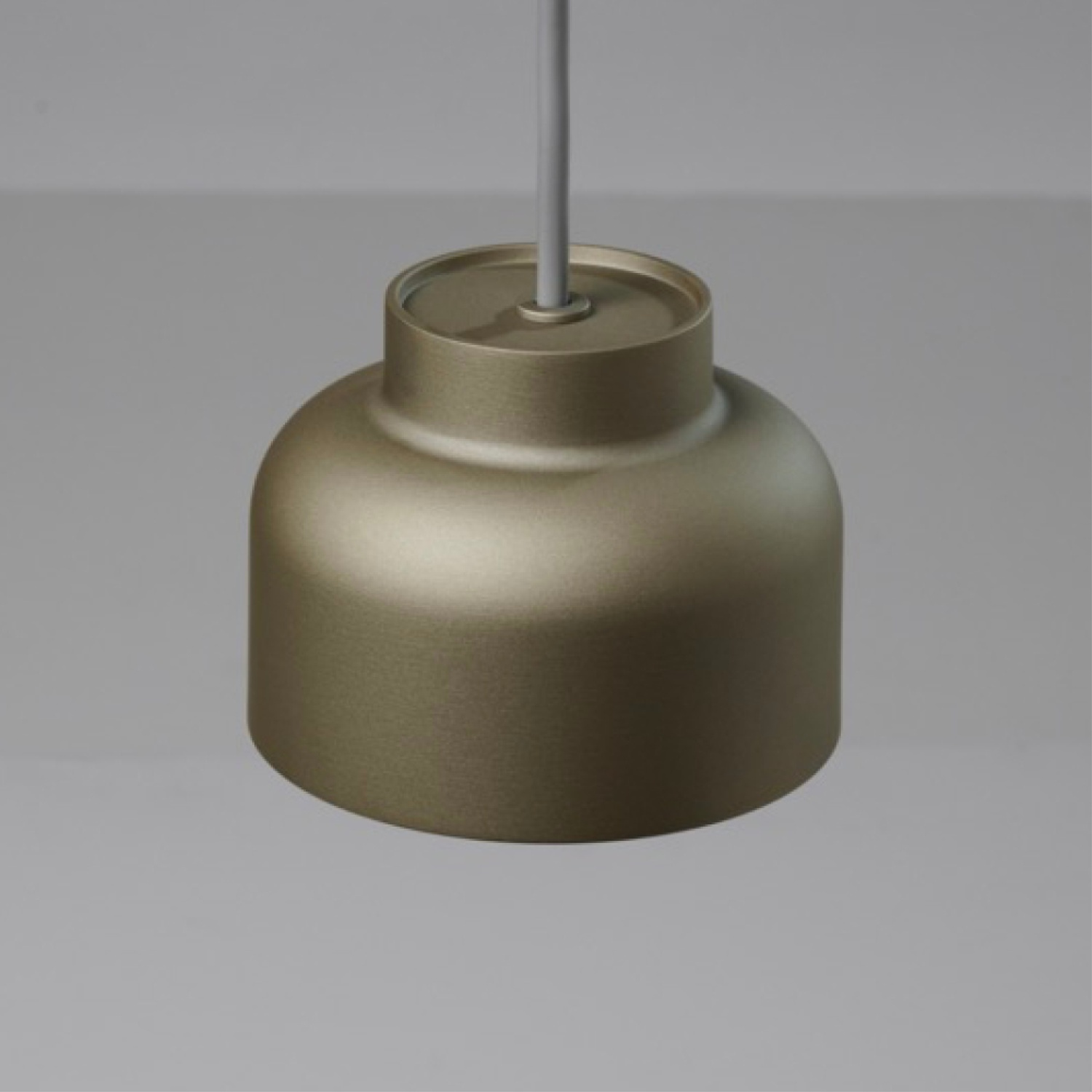 Primo piano di una lampada a sospensione. Forma cilindrica, colore bronzo, appesa a un soffitto bianco.