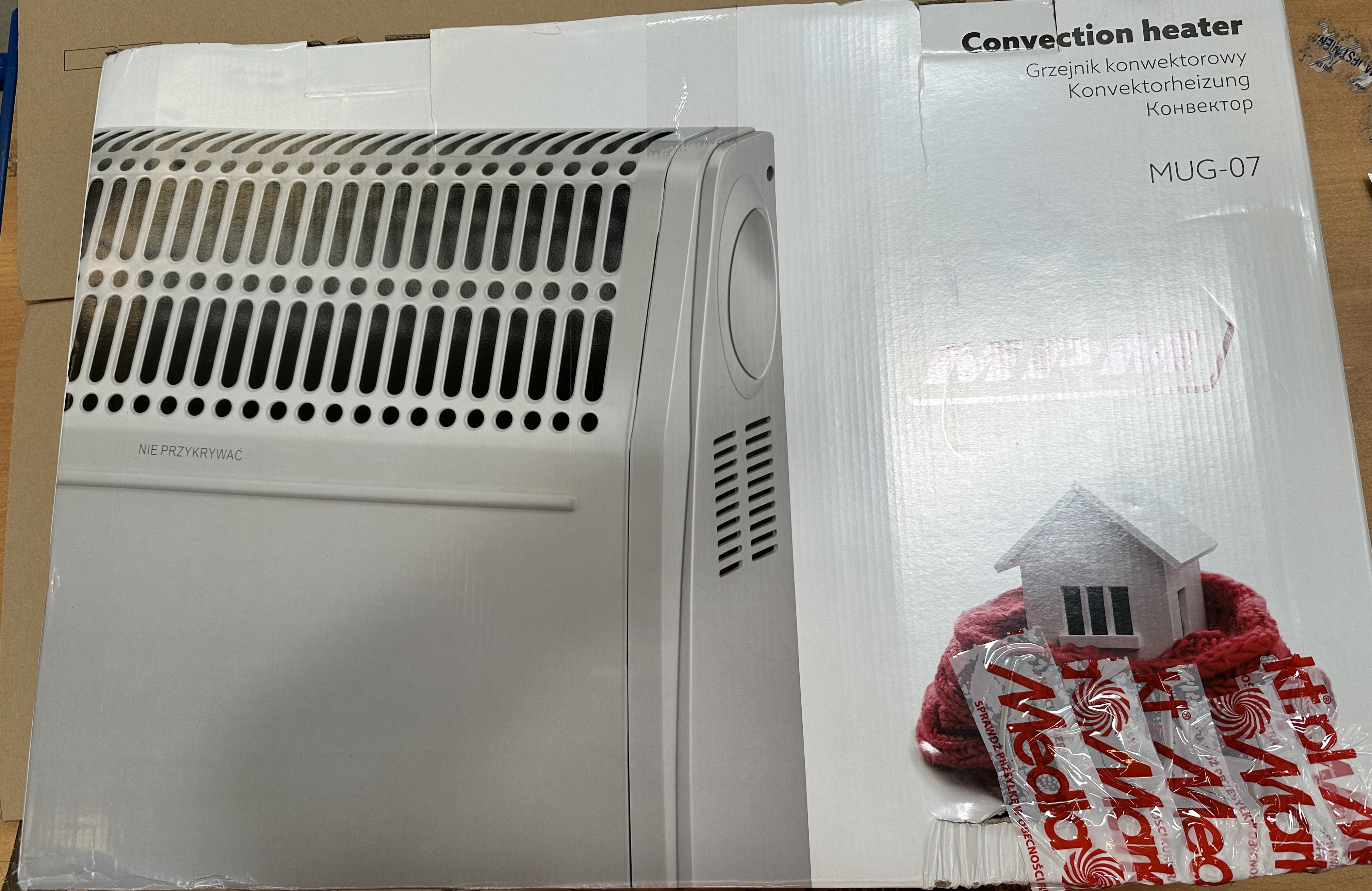 Zapakowany biały grzejnik konwekcyjny z małym domkiem i szalikiem z przodu.