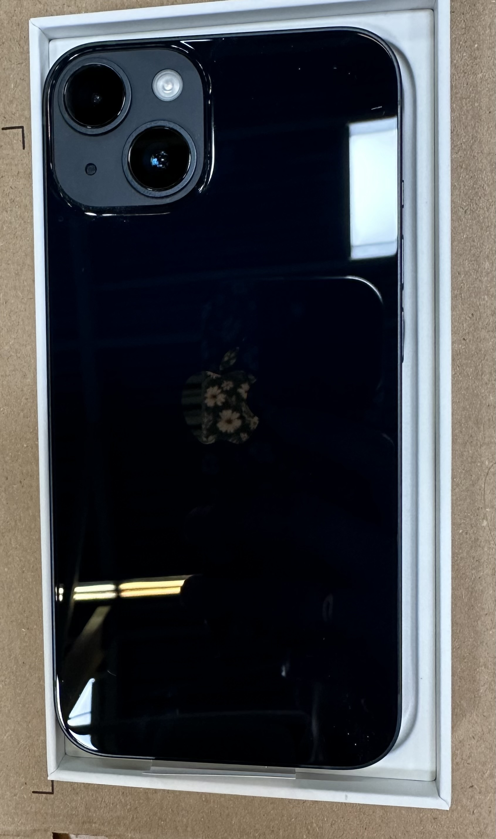 Czarny smartfon w pudełku, widok z tyłu. Posiada moduł kamery i logo Apple.