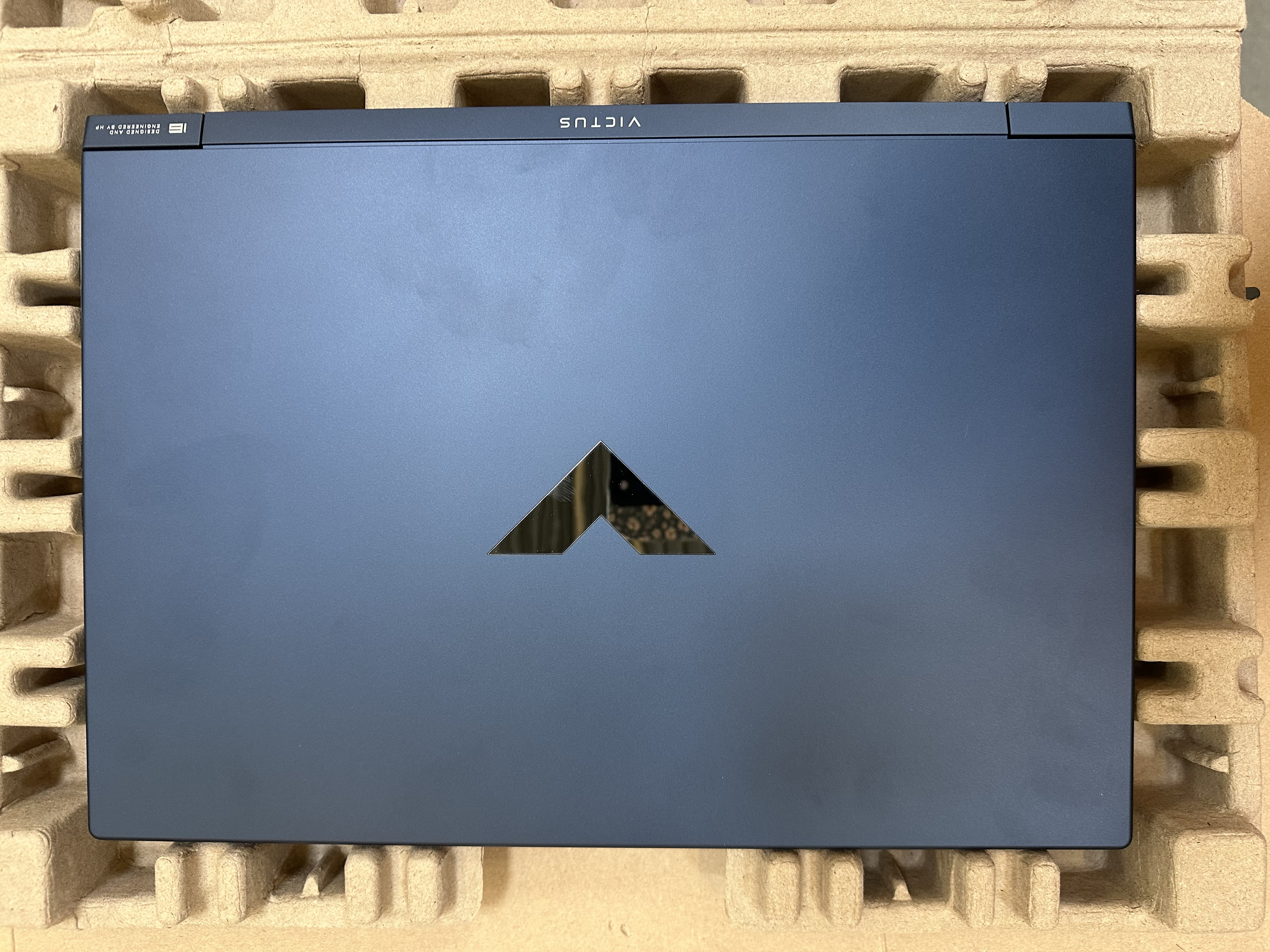 Czarny laptop wewnątrz kartonowego pudełka. Laptop ma logo V.