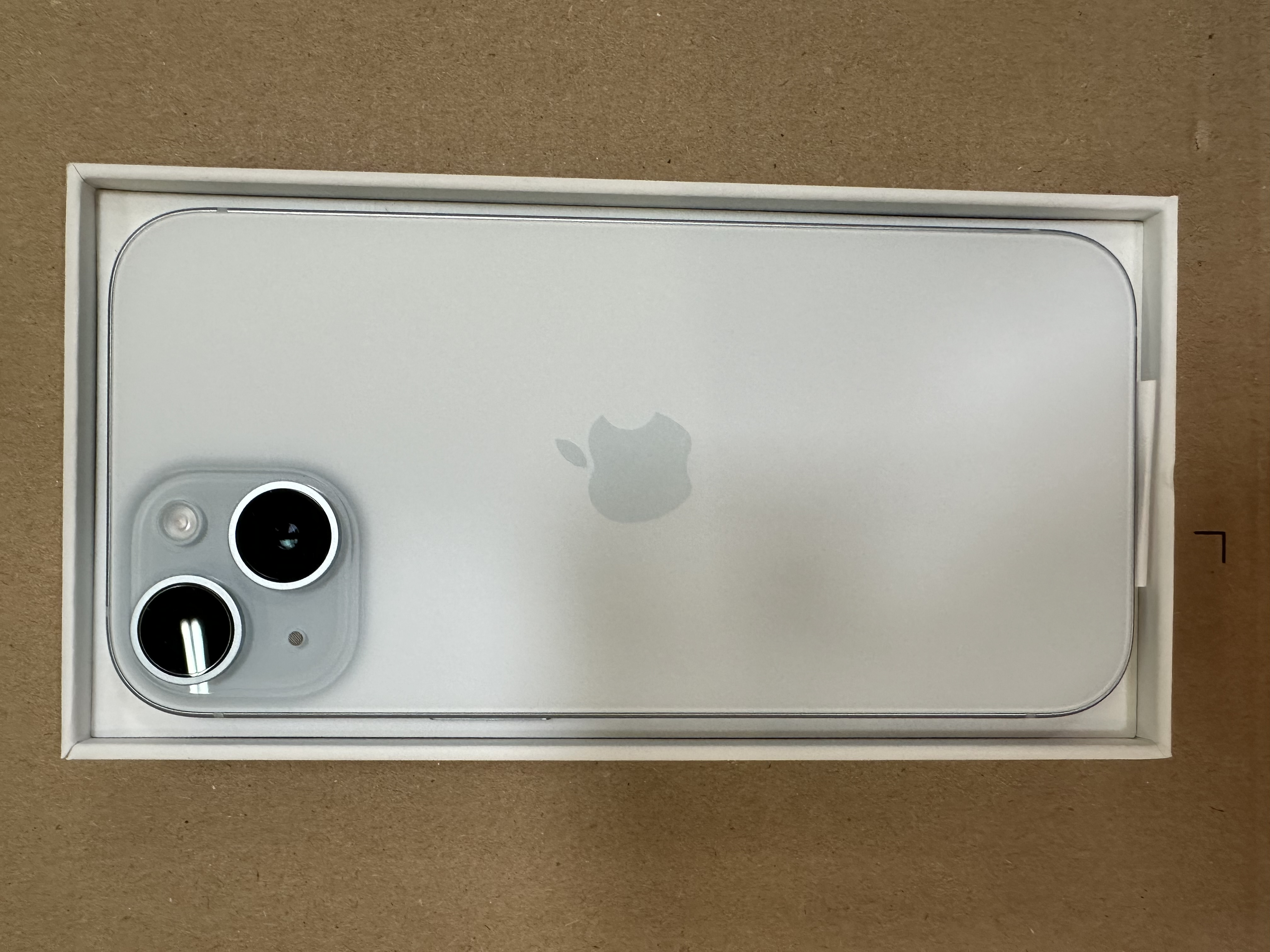 Smartfon w pudełku, tyłem do góry. Telefon jest srebrny i ma aparat fotograficzny.
