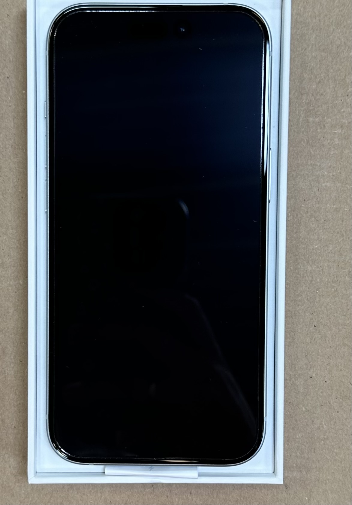 Czarny telefon w białym pudełku na brązowej powierzchni. Ekran jest czarny i wyłączony.