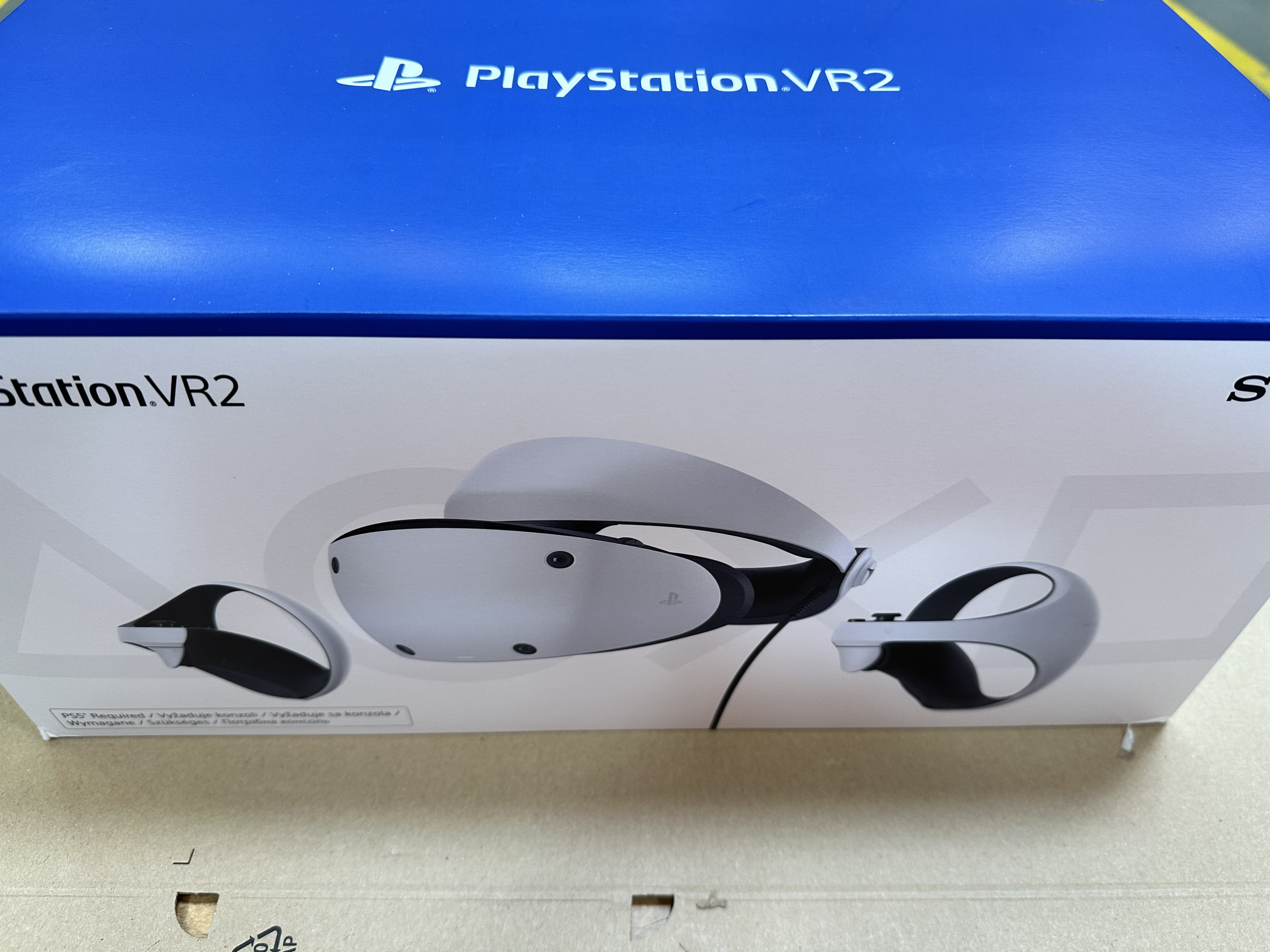 Pudełko PlayStation VR2. Biały zestaw VR i kontrolery. Niebieska góra pudełka z logo i nazwą produktu.