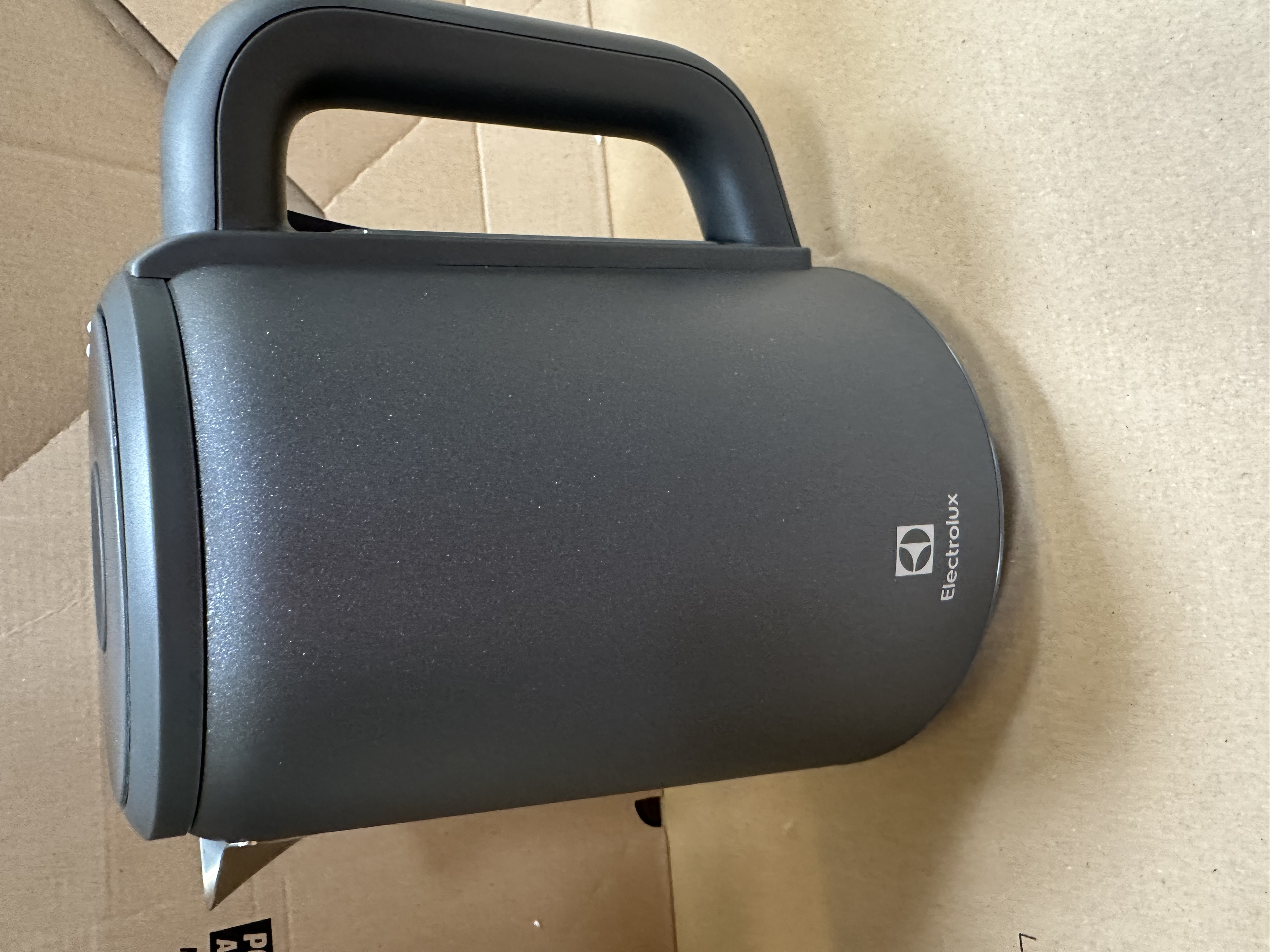 Ciemnoszary sprzęt Electrolux z uchwytem, na brązowej powierzchni kartonowej. Widoczne logo.