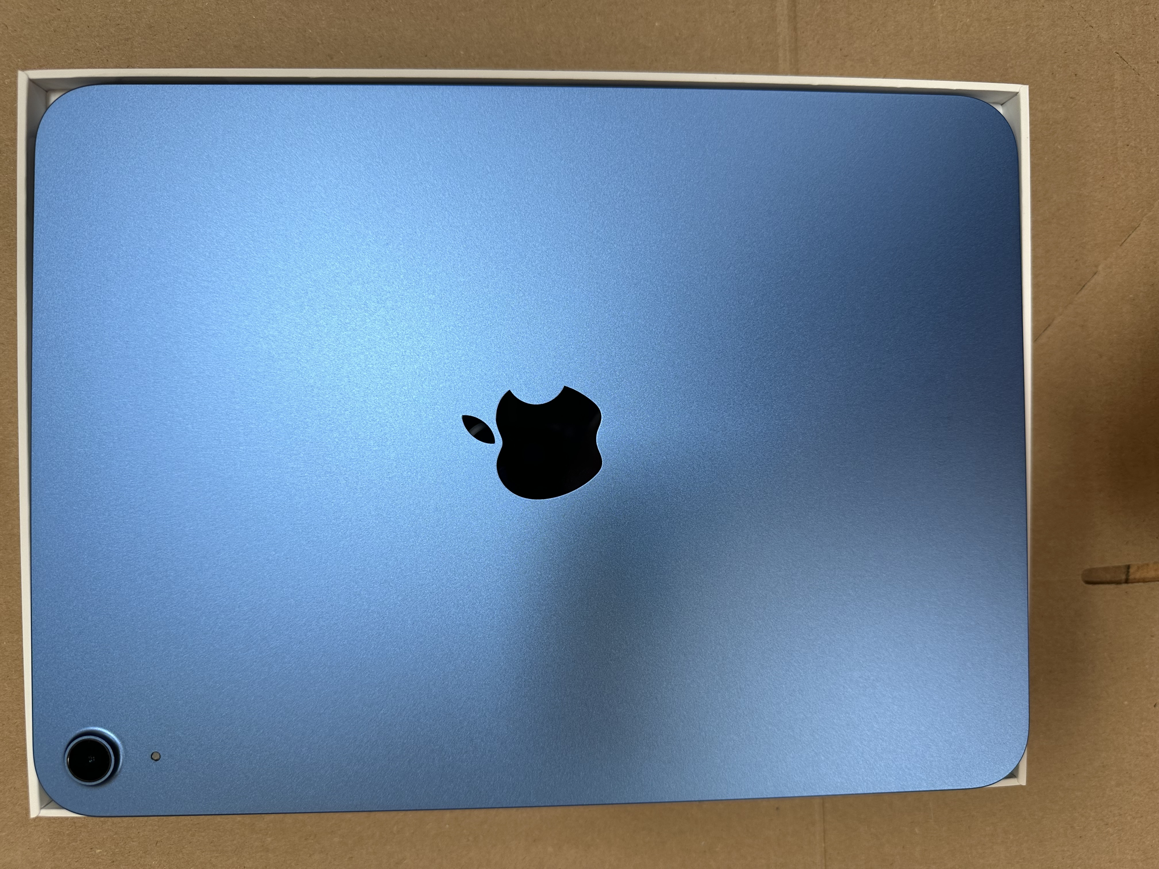 Niebieski iPad Apple w białym pudełku. Tło to brązowy karton.